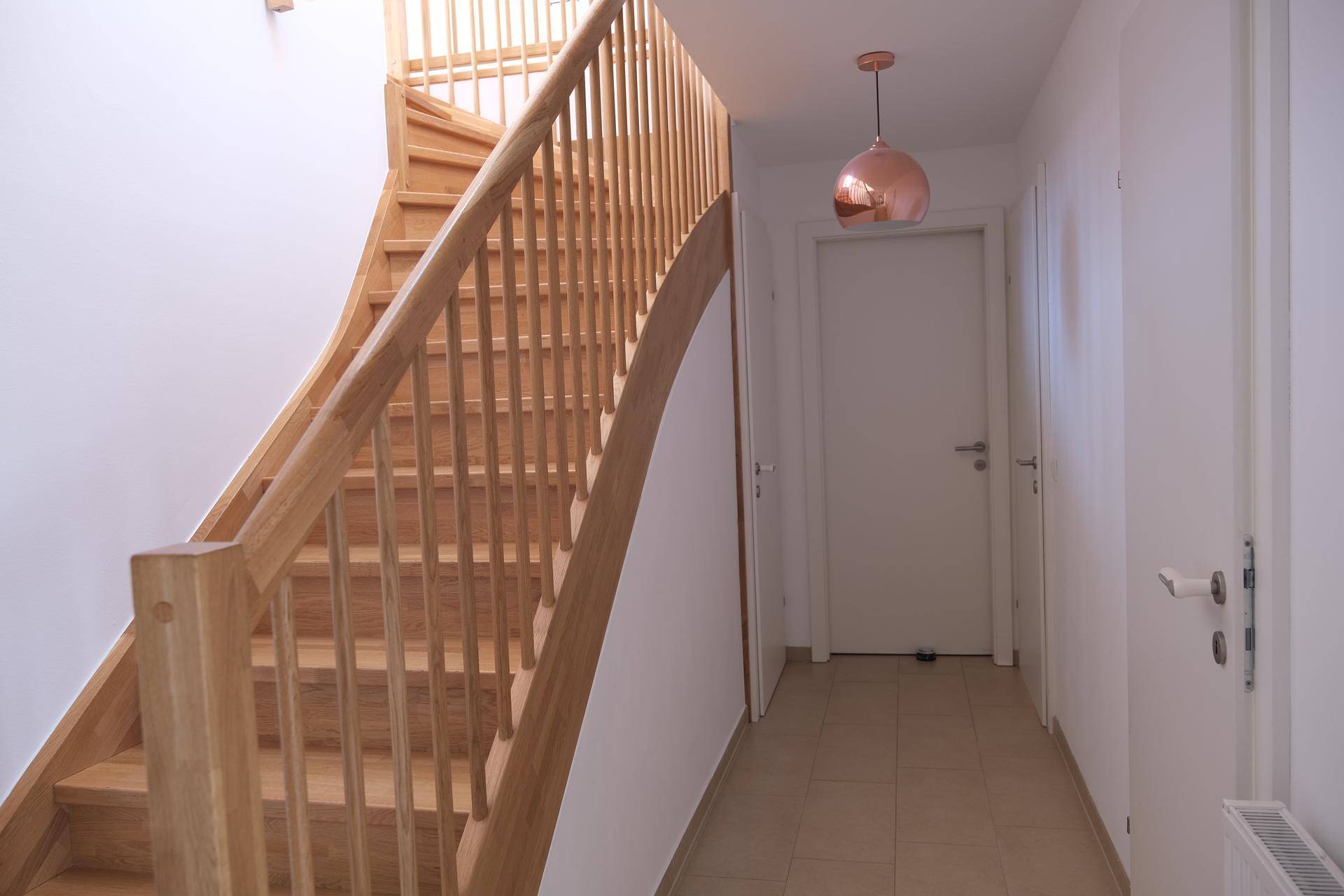 Geräumiger Flur mit heller Holztreppe und weißen Türen, die zu weiteren Räumen führen.