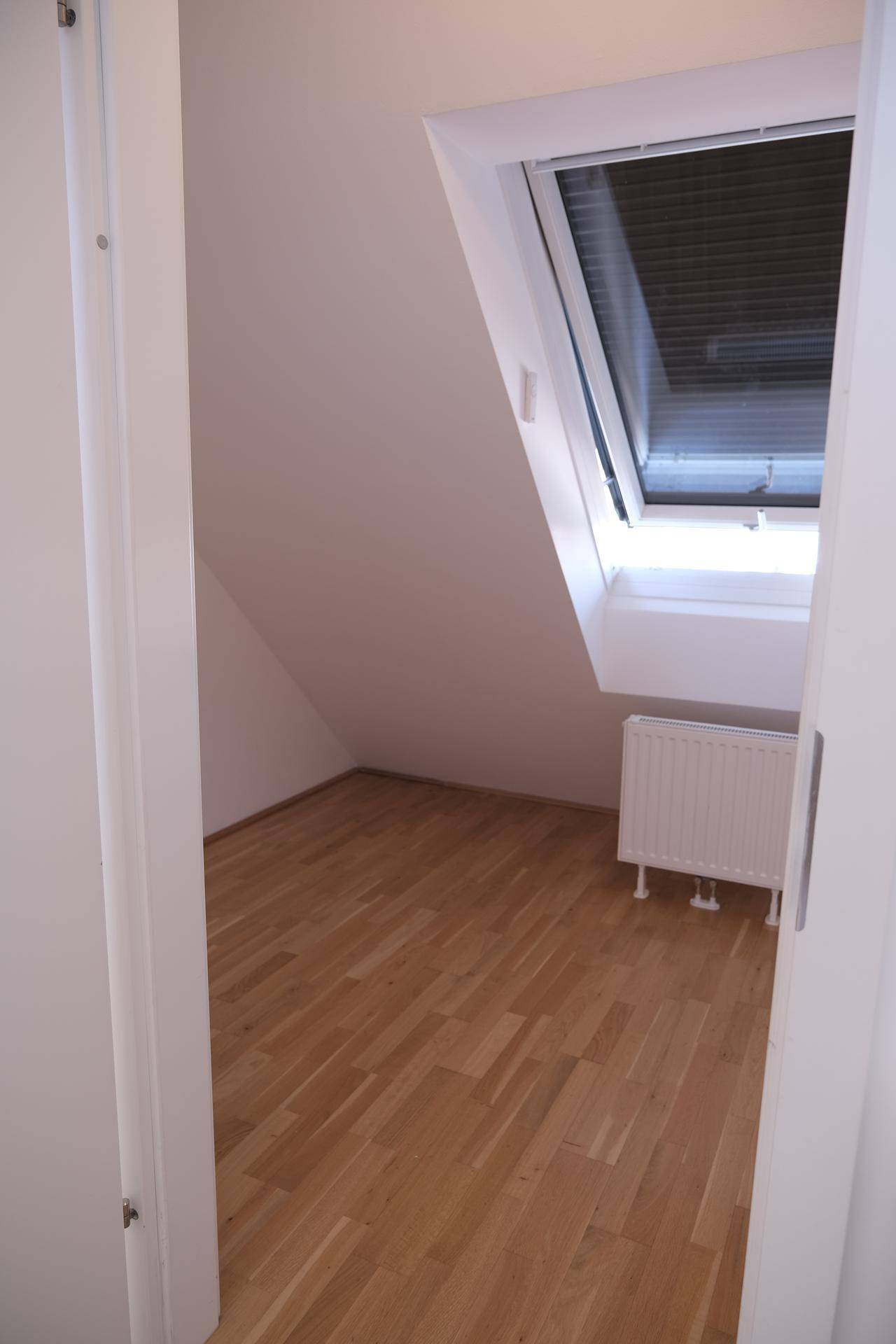 Heller, leerer Raum im Dachgeschoss mit Holzboden und einem großen Dachfenster.