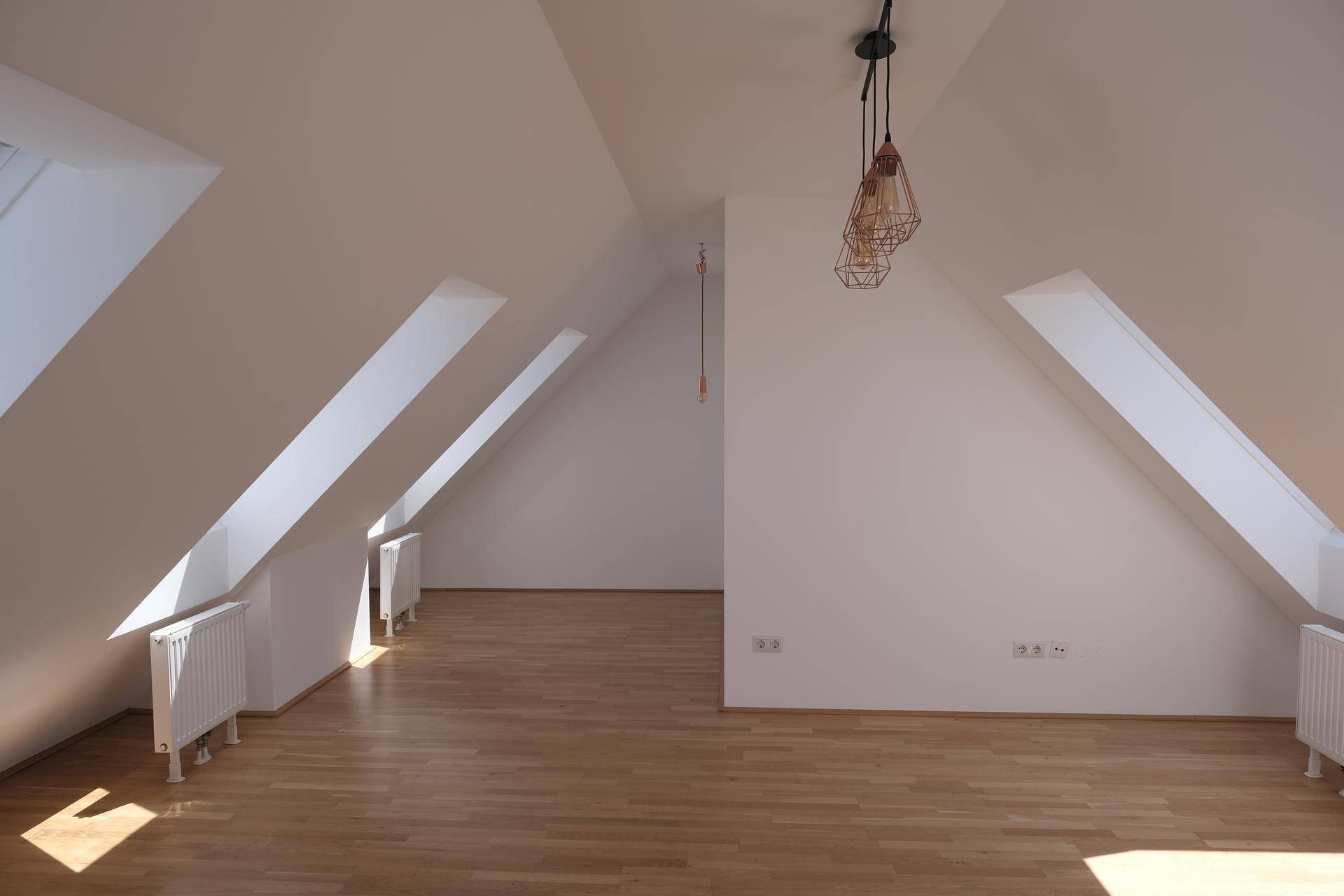Heller, leerer Wohnbereich im Dachgeschoss mit Holzboden und schrägen Wänden.