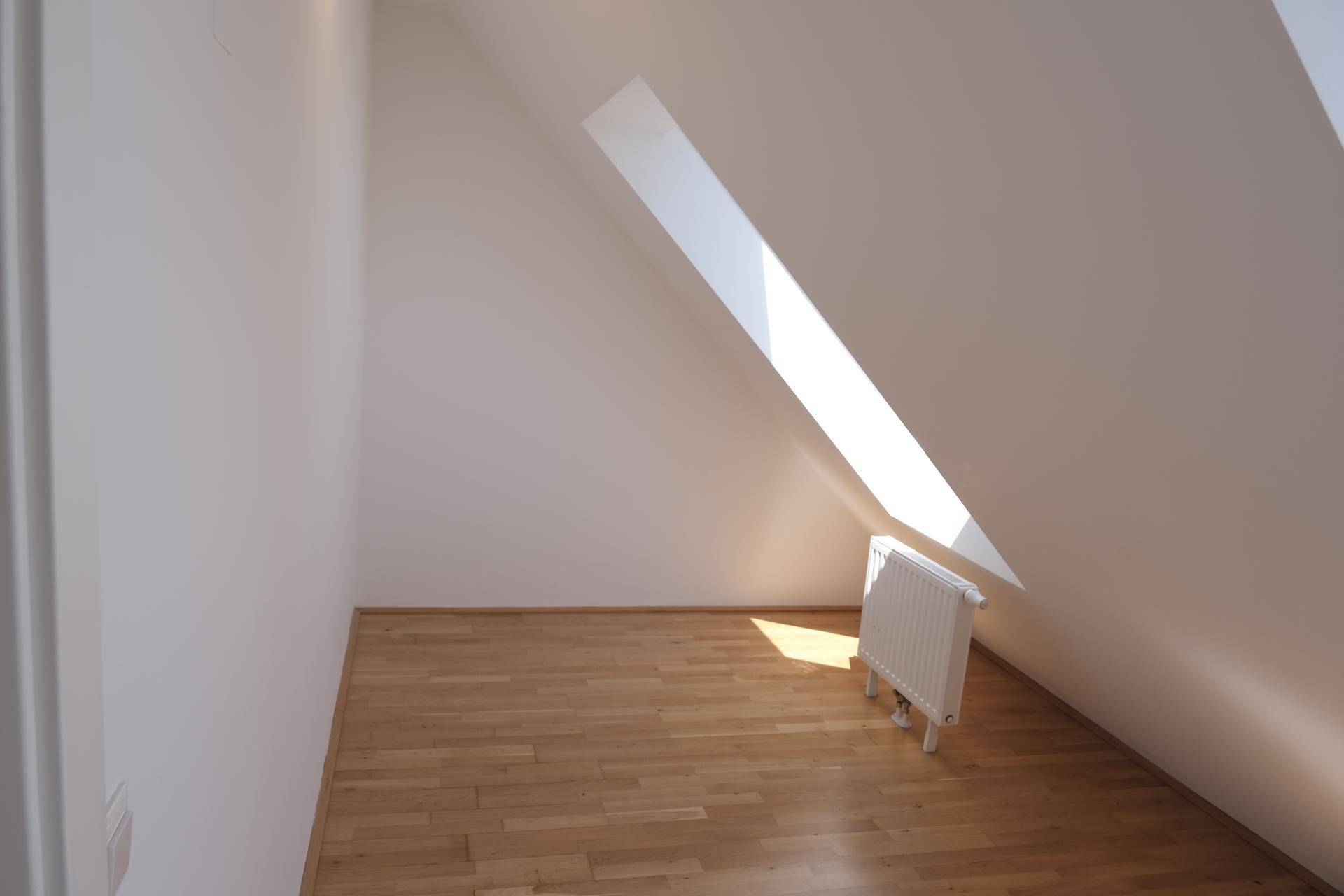 Heller, leerer Raum im Dachgeschoss mit Holzboden und schrägem Dachfenster.