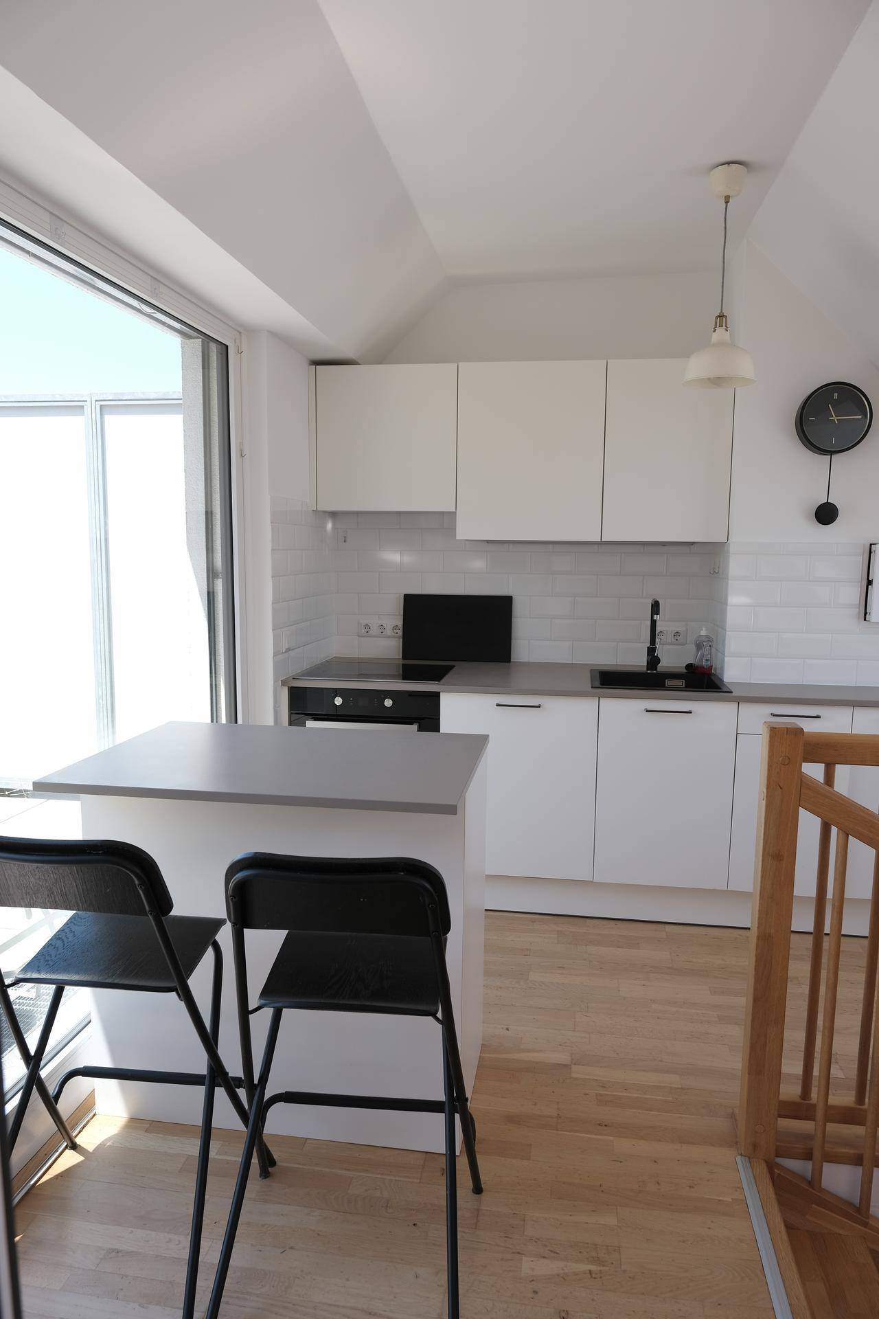 Helle Küchenzeile mit weißen Fronten, kleiner Insel und direktem Zugang zur Dachterrasse.