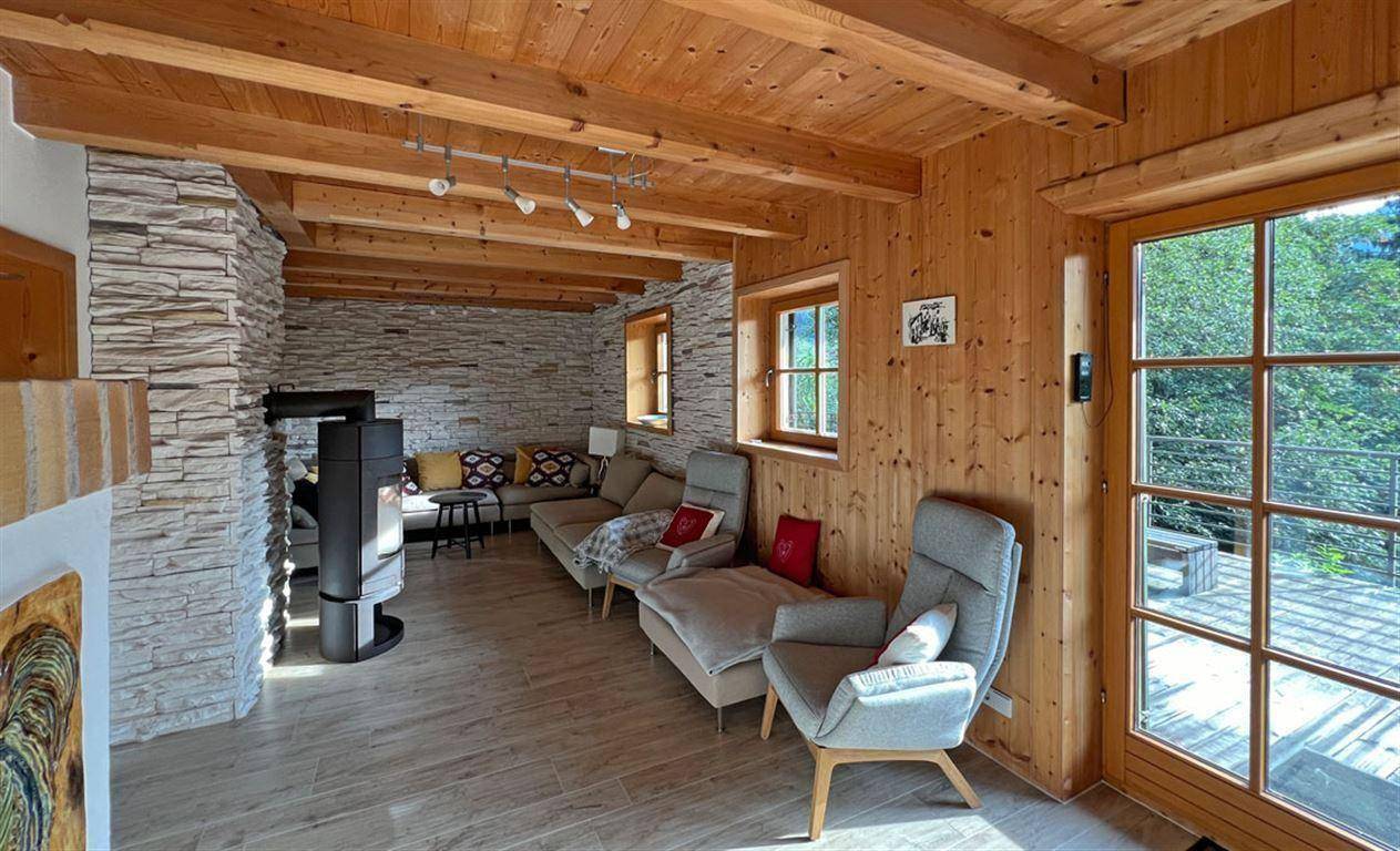 Rustikales Wohnzimmer mit Holzbalkendecke, Steinwand und modernem Holzofen, mit Zugang zur Terrasse.