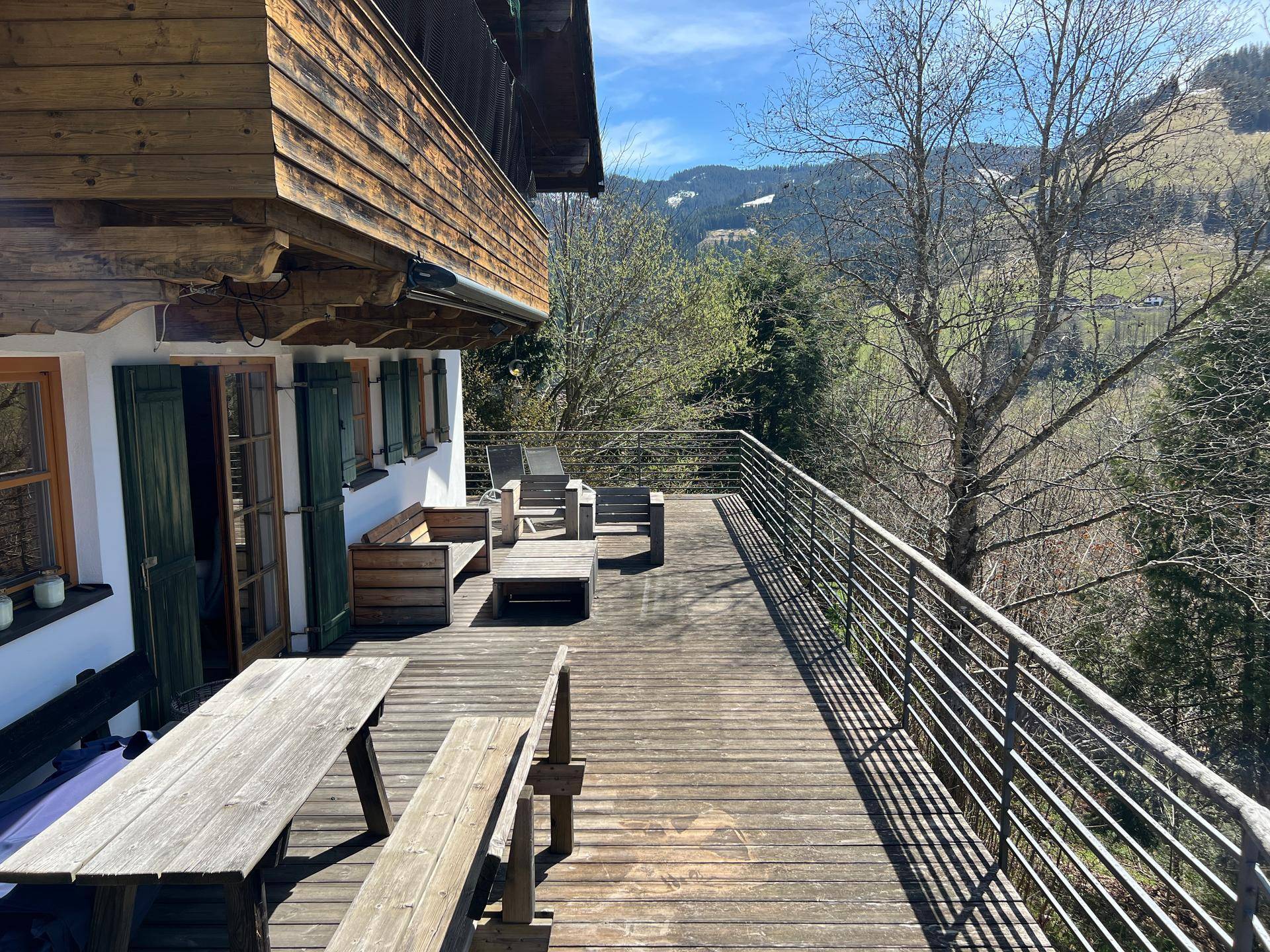 Sonnige Holzterrasse mit rustikalen Möbeln und freiem Blick auf die grünen Hügel und Berge.