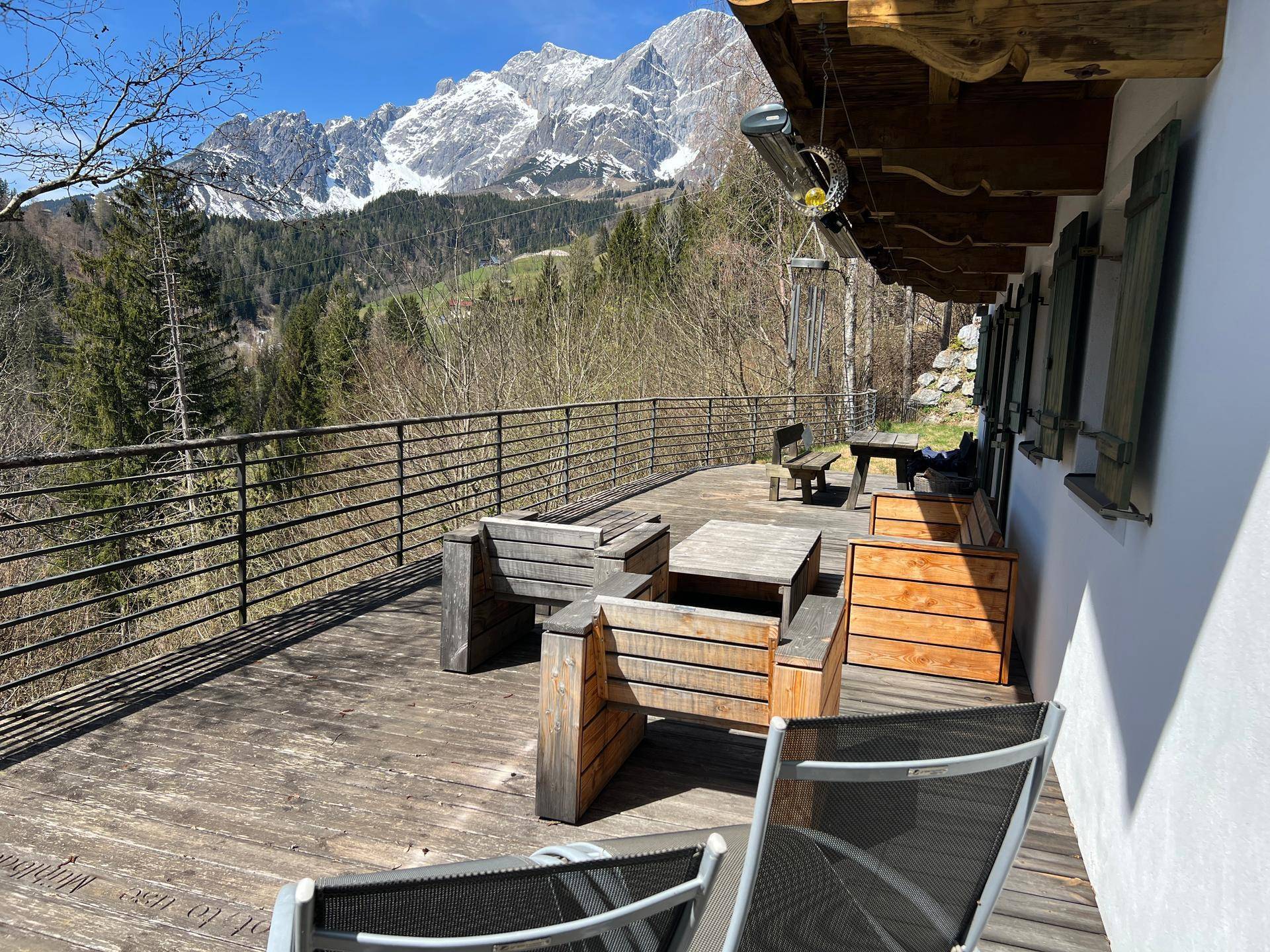 Sonnige Holzterrasse mit Sitzmöbeln und spektakulärem Panoramablick auf die schneebedeckten Berge.
