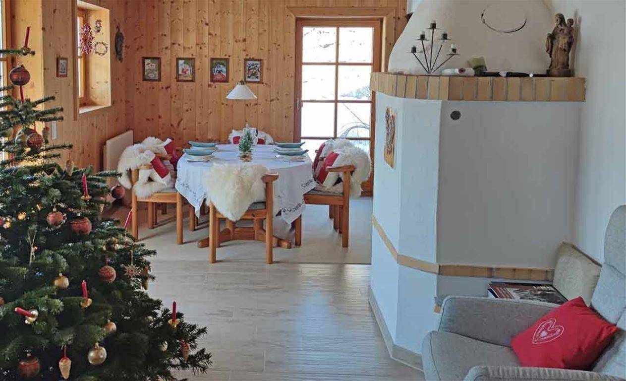 Gemütlicher Essbereich mit traditionellem Kachelofen, Holzwänden und festlich geschmücktem Weihnachtsbaum.