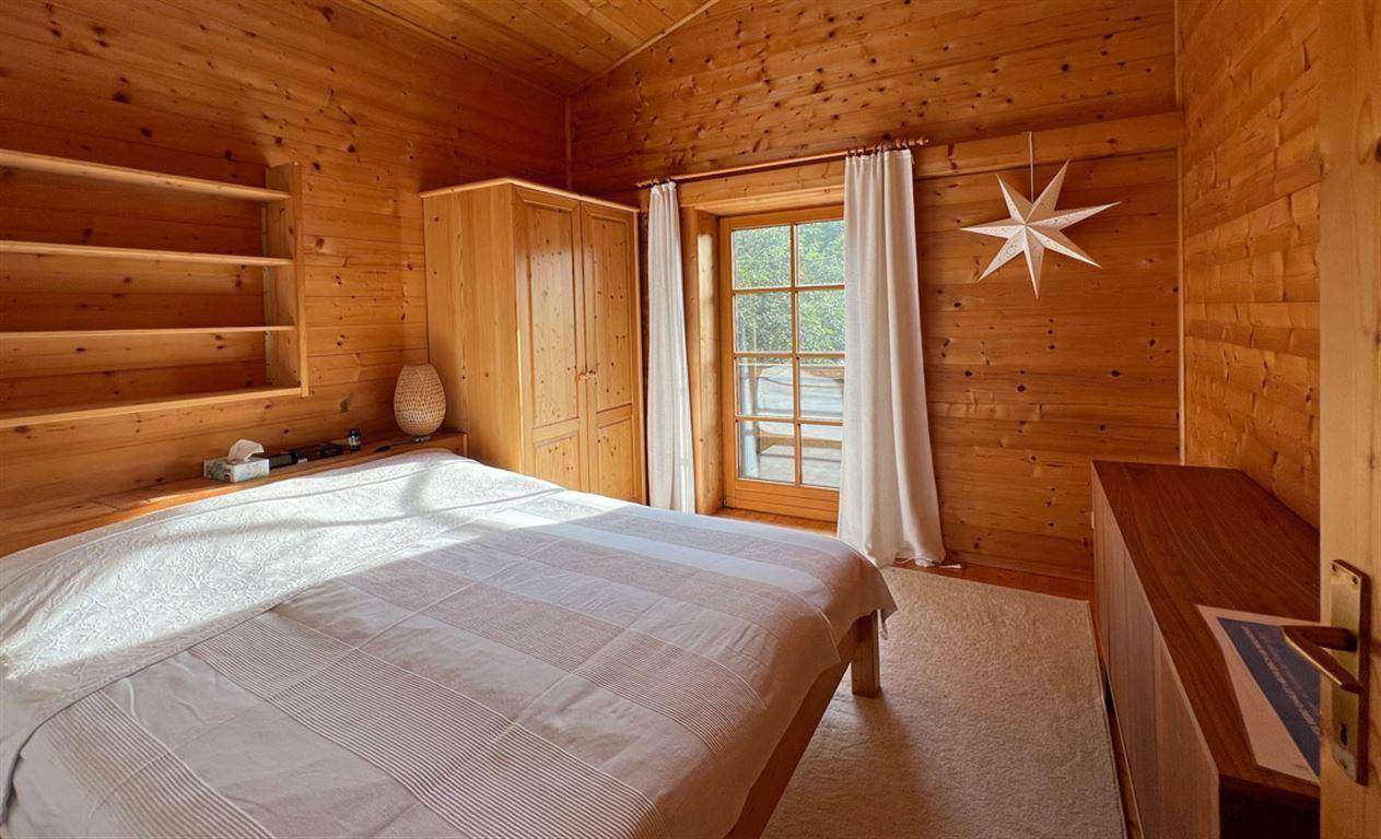 Gemütliches Schlafzimmer mit Holzwänden, Holzboden und Zugang zu einem Balkon.