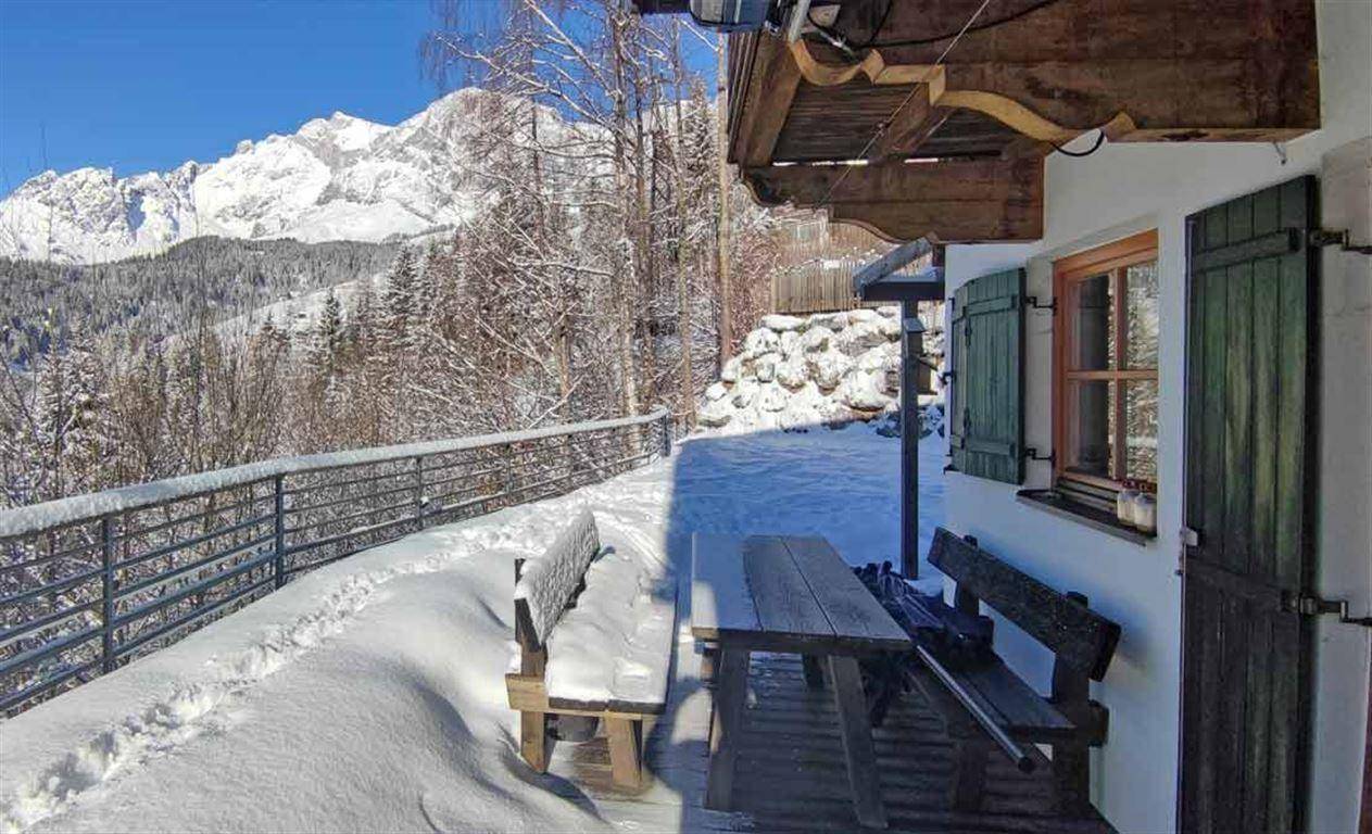 Verschneite Terrasse mit rustikalen Holzmöbeln und atemberaubendem Panoramablick auf die winterlichen Berge.