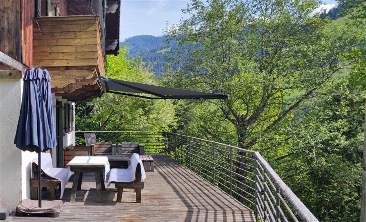 Geräumige Holzterrasse mit Sitzgelegenheiten, Sonnenschirm und weitem Blick auf die grüne Berglandschaft.