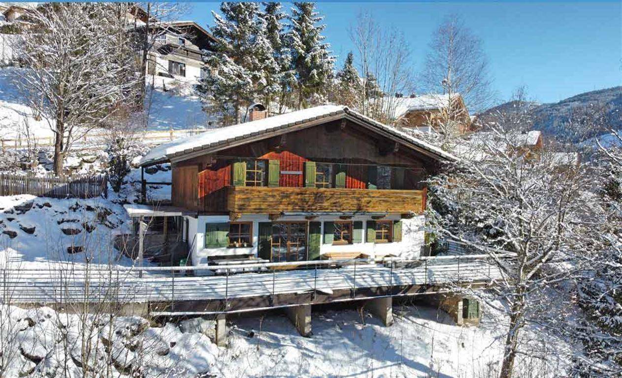 Traditionelles Chalet in verschneiter Berglandschaft mit Holzbalkon und grünen Fensterläden.