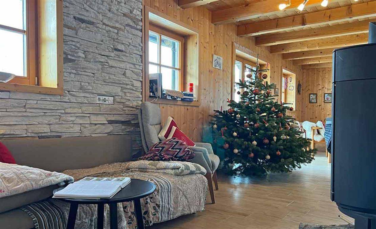 Geräumiges Wohnzimmer mit Holzwänden, Steinakzentwand und Holzofen, geschmückt für die Weihnachtszeit.