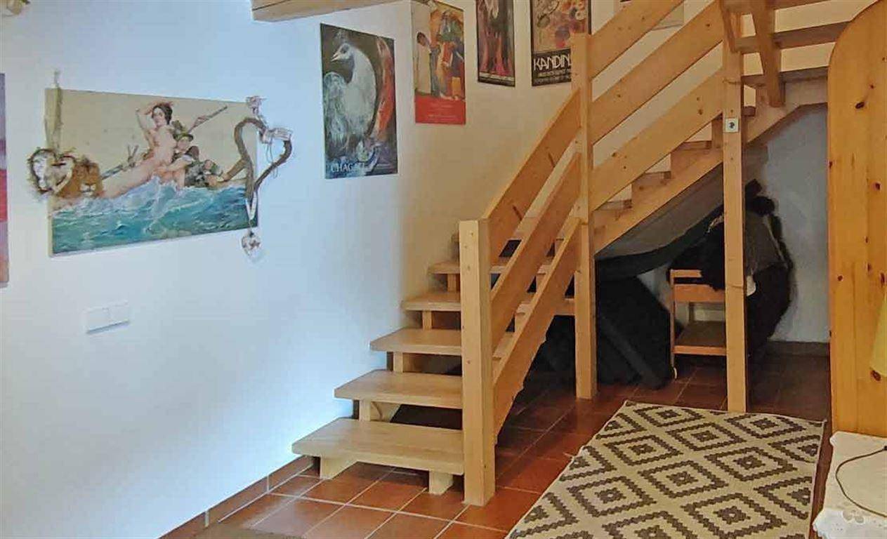 Helles Treppenhaus mit Holztreppe und Fliesenboden, dekoriert mit Kunstwerken an den Wänden.