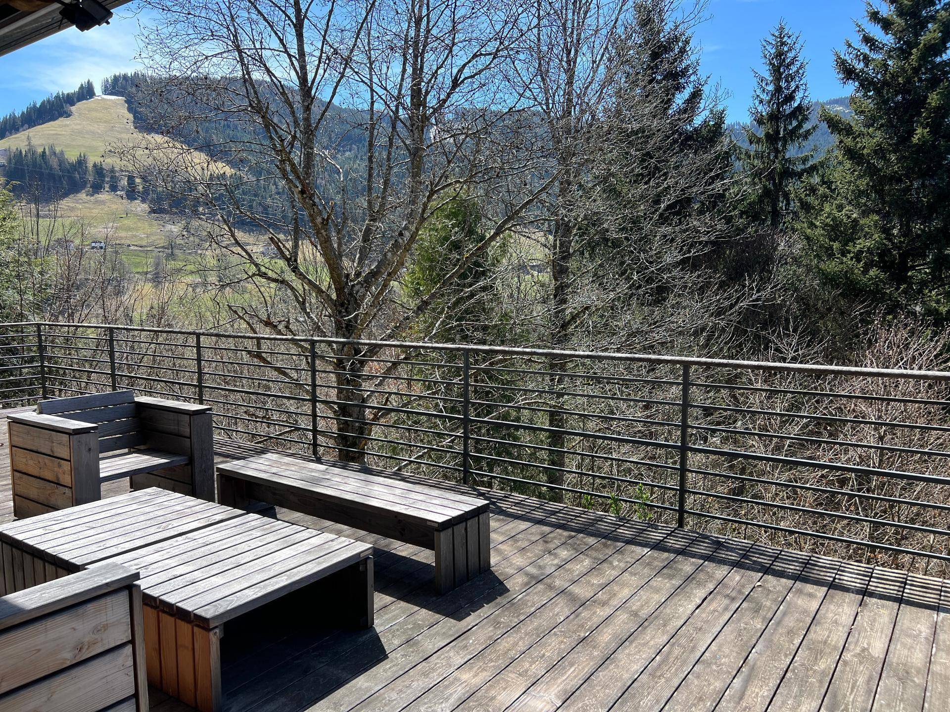 Holzterrasse mit Sitzgelegenheiten und einem weiten Ausblick auf bewaldete Hügel und die Natur.