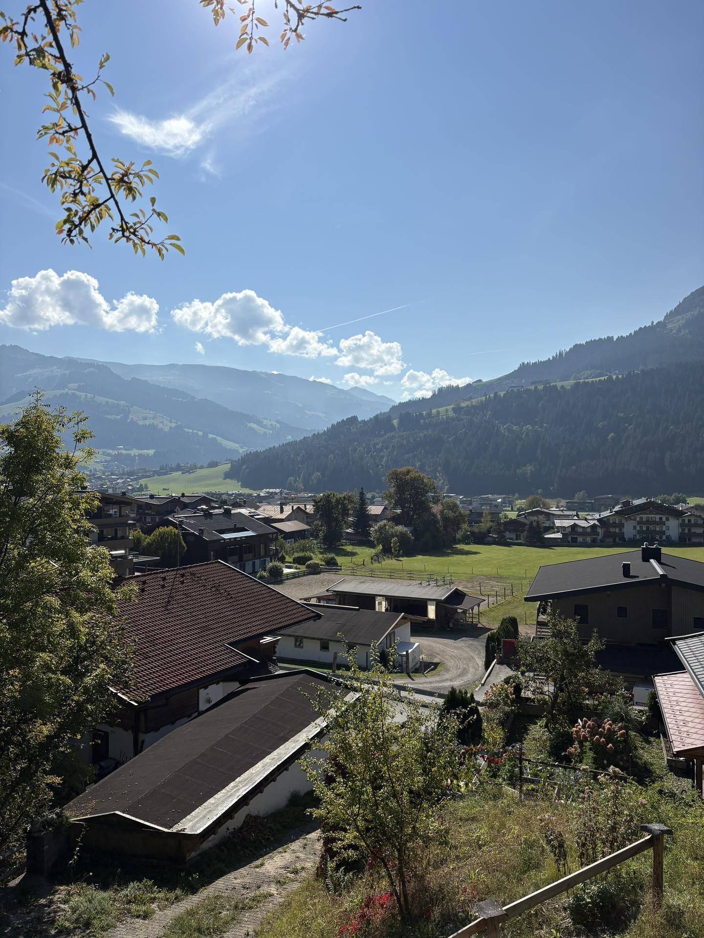 Weitläufiger Blick über eine ländliche Siedlung mit Feldern und Bergen unter klarem Himmel.