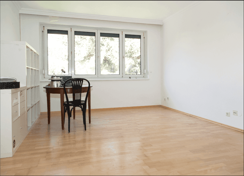 Geräumiges Zimmer mit hellem Holzfußboden, großem Fenster und einem kleinen Arbeitsbereich.