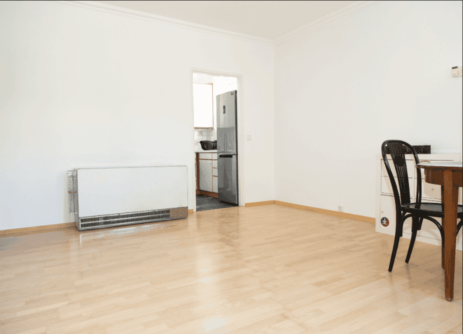Heller Wohnbereich mit Holzfußboden und Zugang zu einer Küche, ausgestattet mit einem Kühlschrank.