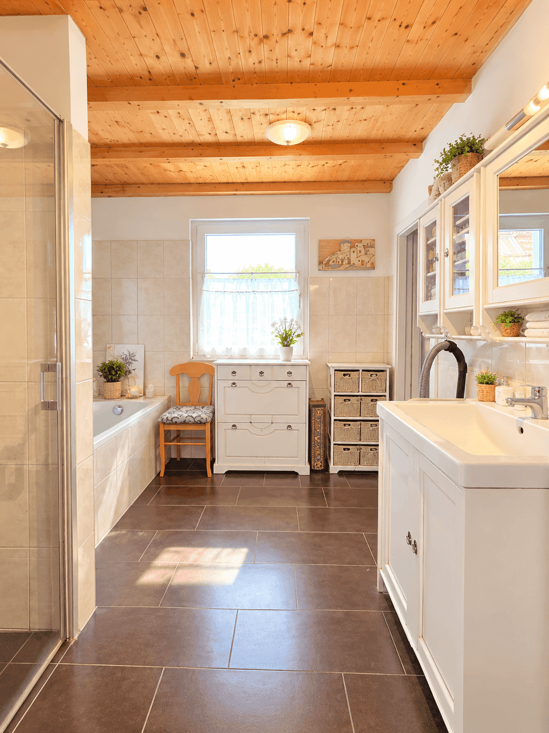 Helles Badezimmer mit Badewanne, Dusche, Fenster und Holzbalkendecke.