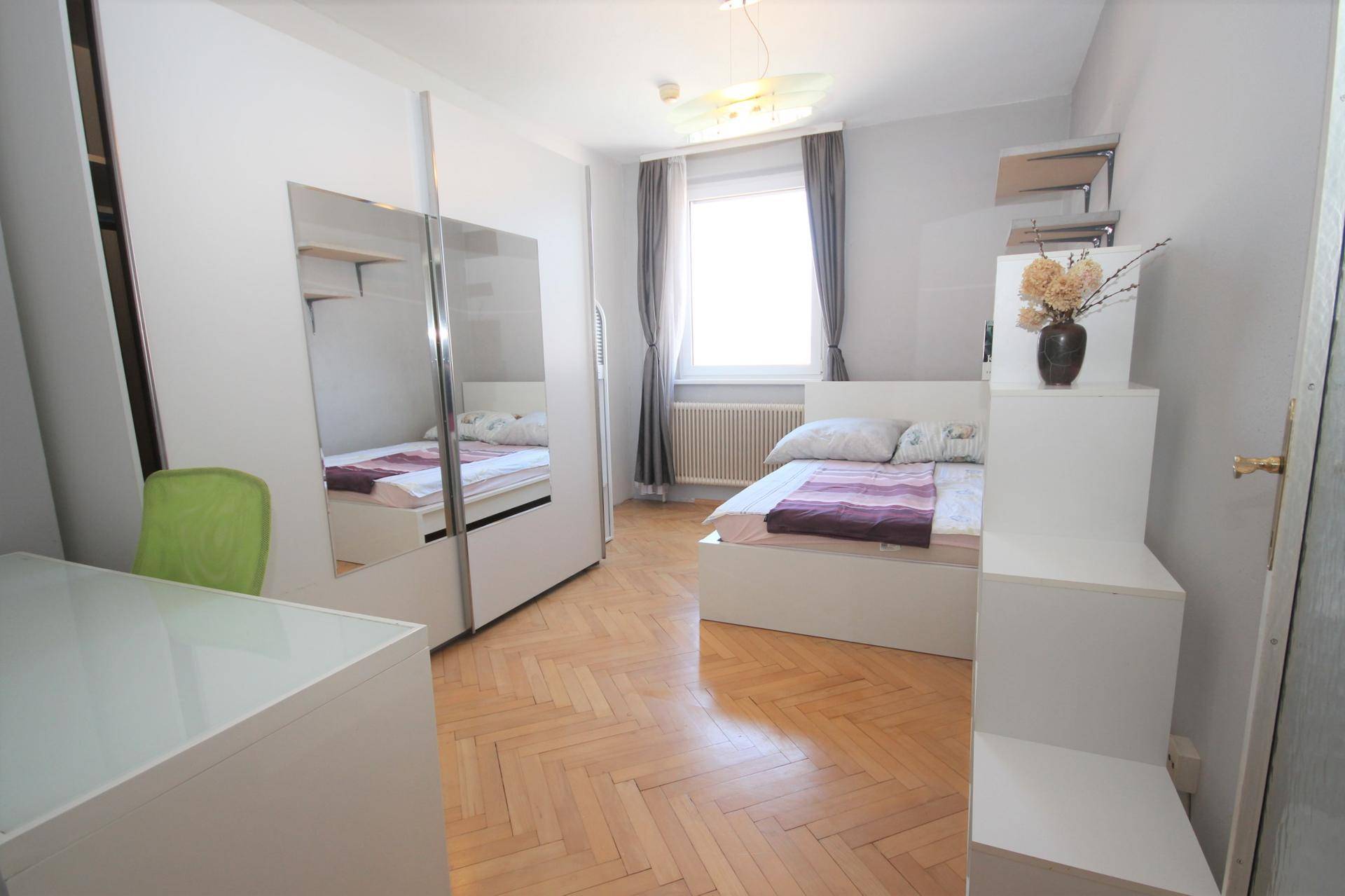 Helles Schlafzimmer mit Bett, Spiegelschrank und Parkettboden.