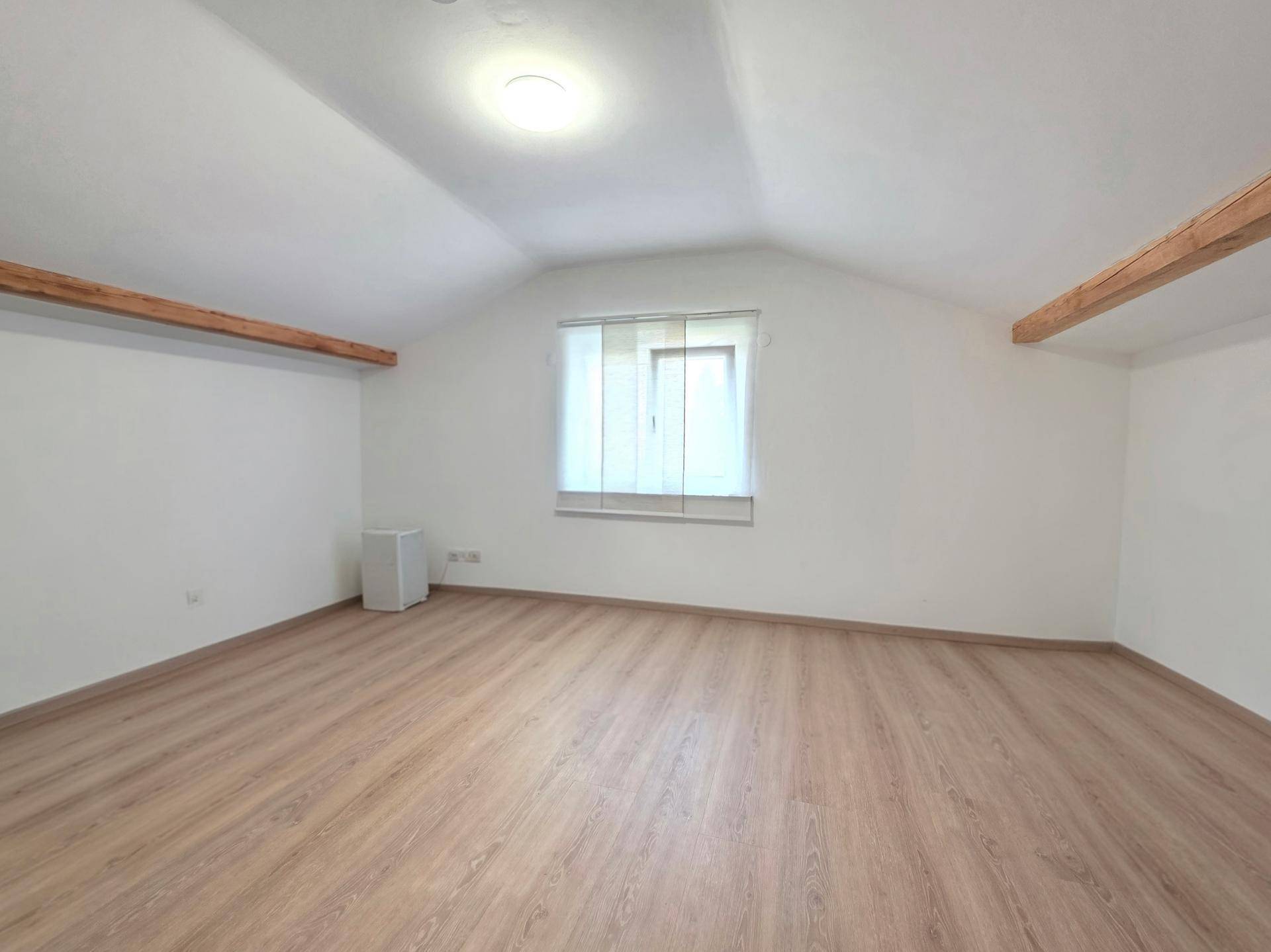 Helles Gästezimmer im Dachgeschoss mit Laminatboden und Fenster.