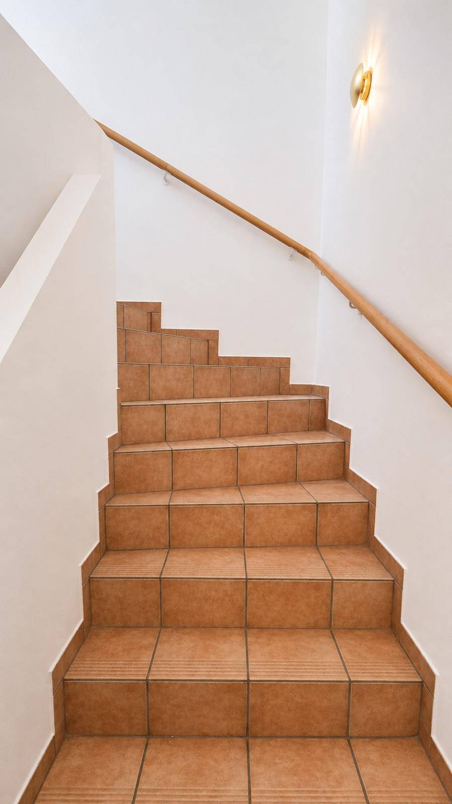 Geflieste Treppe mit Holzgeländer, die in ein oberes Stockwerk führt.