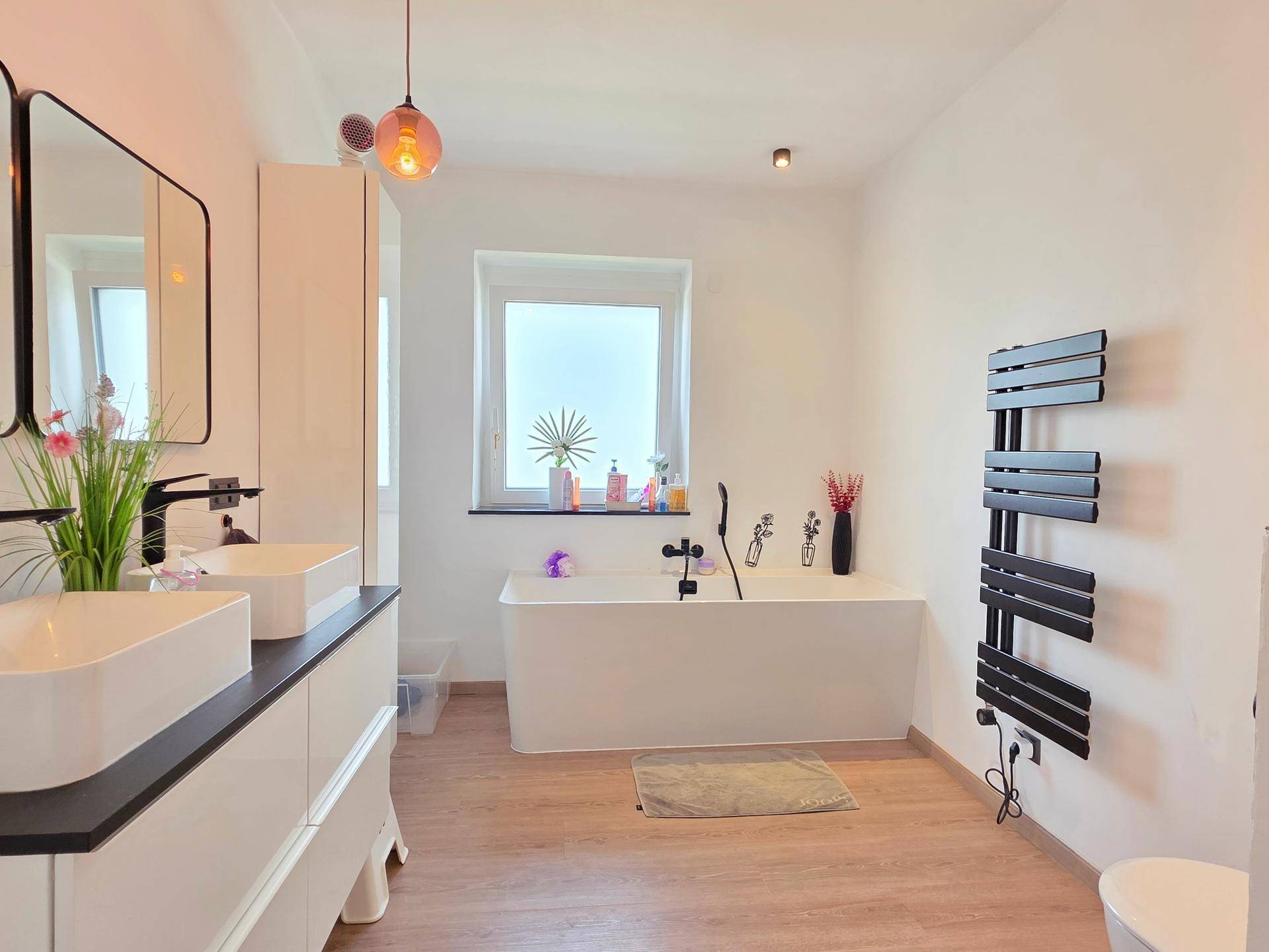Modernes Badezimmer mit freistehender Badewanne, Doppelwaschbecken und Fenster.