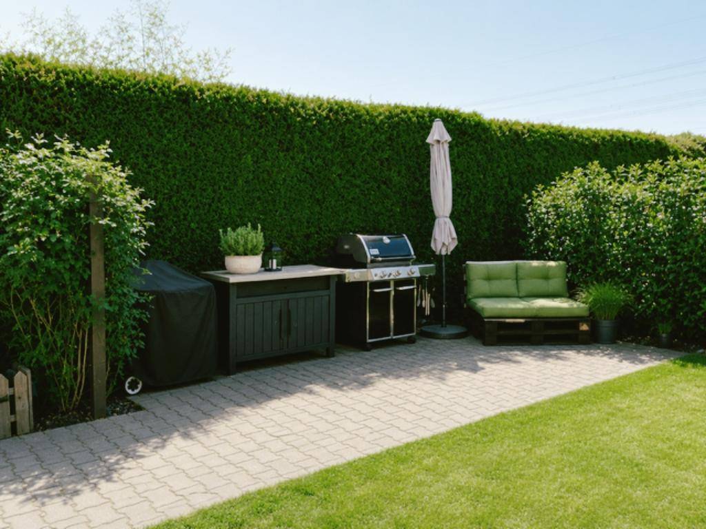 Gemütlicher Grillbereich im Garten mit Sitzgelegenheiten und hoher Hecke für Privatsphäre.