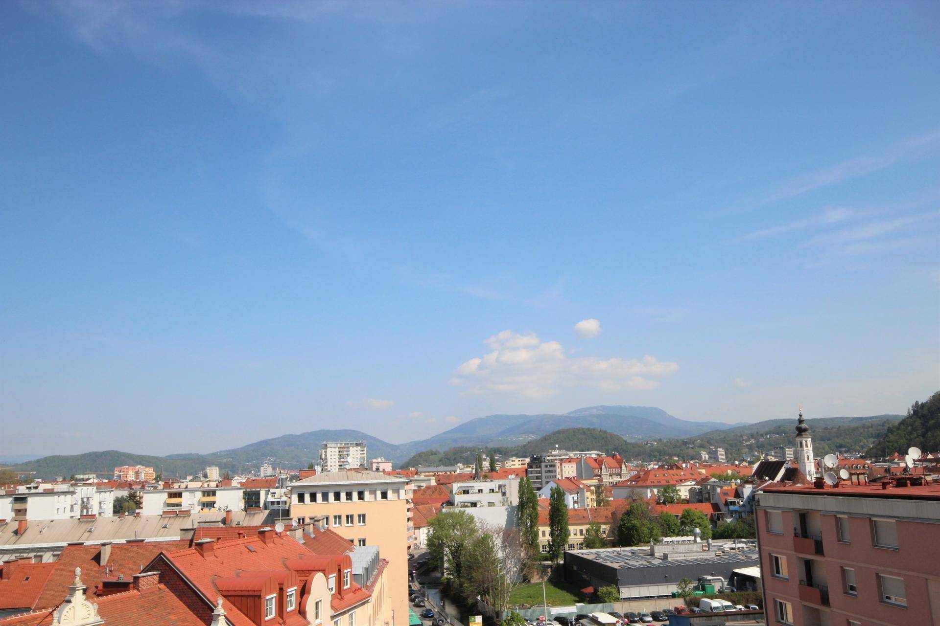Weitläufiger Blick über die Stadt mit Bergen im Hintergrund unter klarem Himmel.