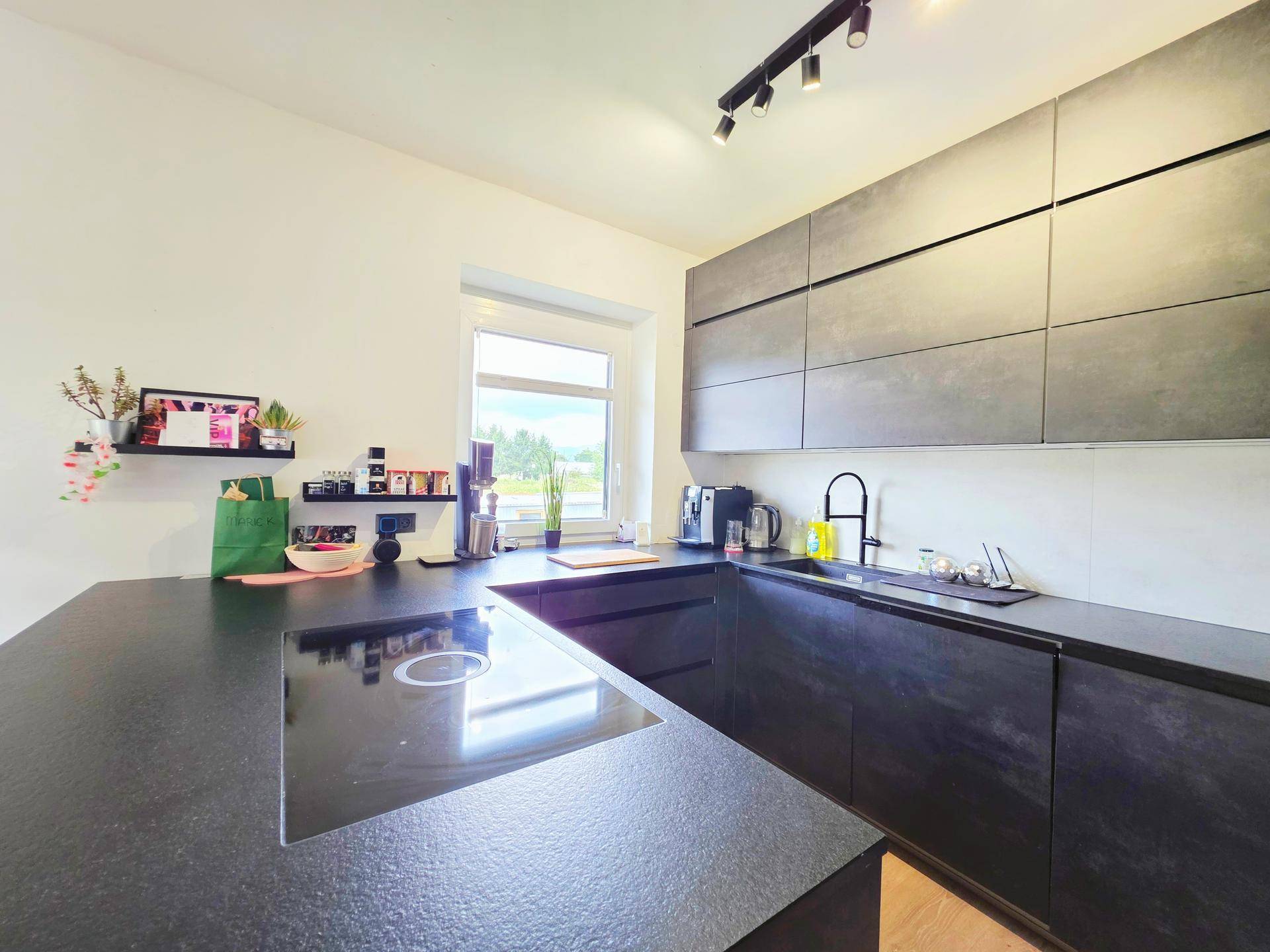 Moderne Küche mit dunklen Arbeitsplatten, Induktionskochfeld und Fenster mit Ausblick.