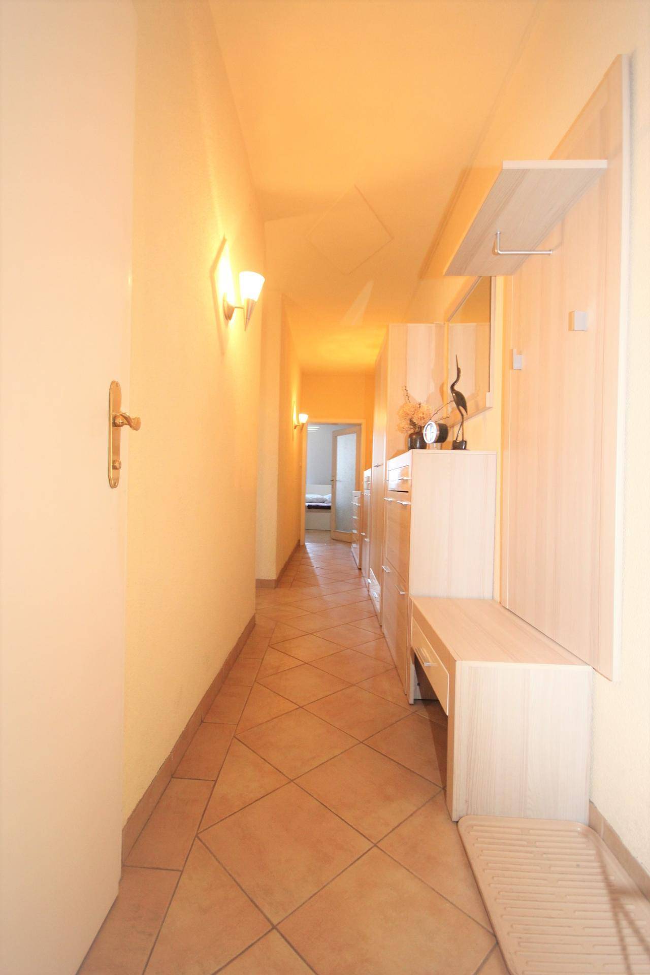 Langer Flur mit hellen Fliesen, Garderobe und indirekter Beleuchtung.