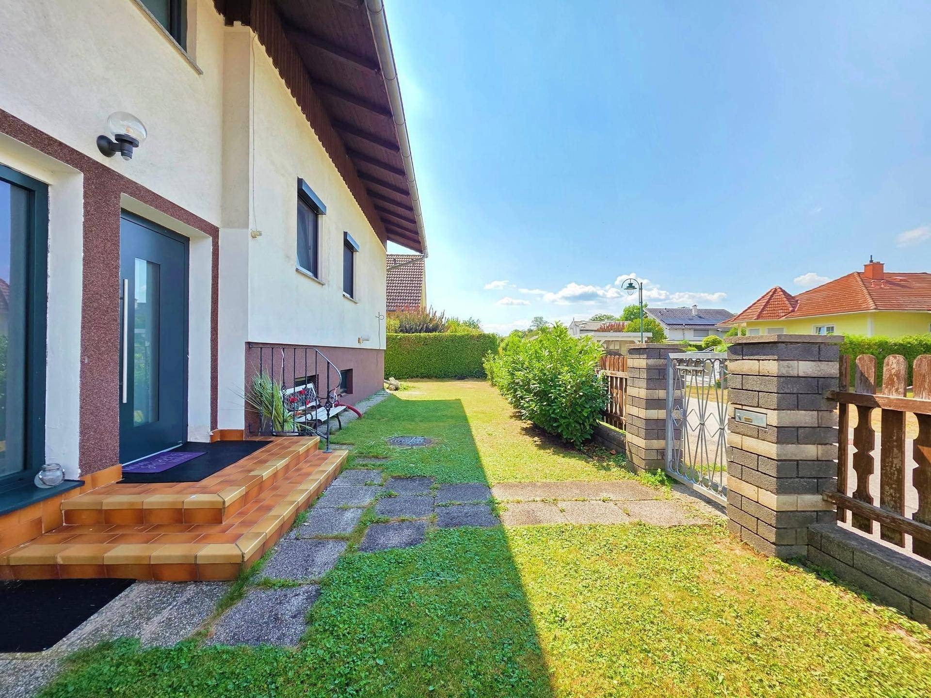 Eingangsbereich eines Hauses mit gepflastertem Weg, Rasenfläche und einem Zaun.