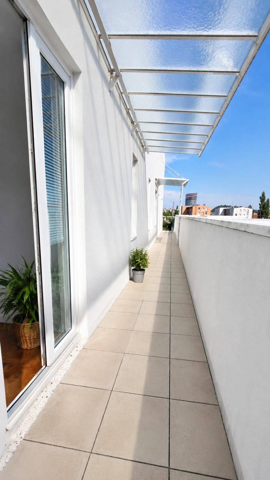 Langer, schmaler Balkon mit Fliesenboden und Glasüberdachung, ideal für Entspannung.