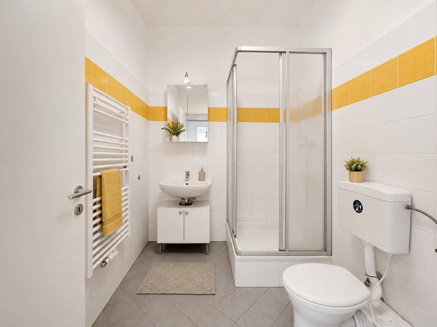 Helles Badezimmer mit Duschkabine, WC, Waschbecken und gelben Akzentfliesen.