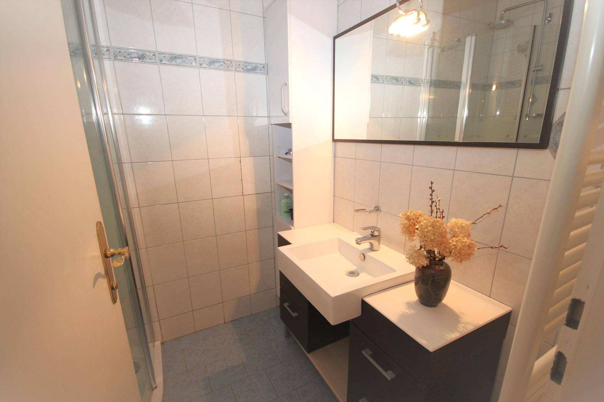 Modernes Badezimmer mit Duschkabine, Waschbecken und Wandspiegel.