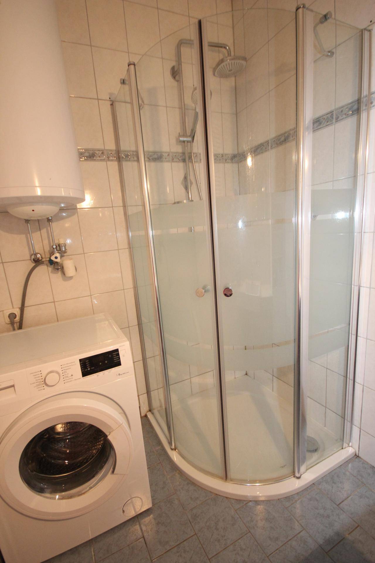 Badezimmer mit Duschkabine und Waschmaschine, gefliest in hellen Farben.