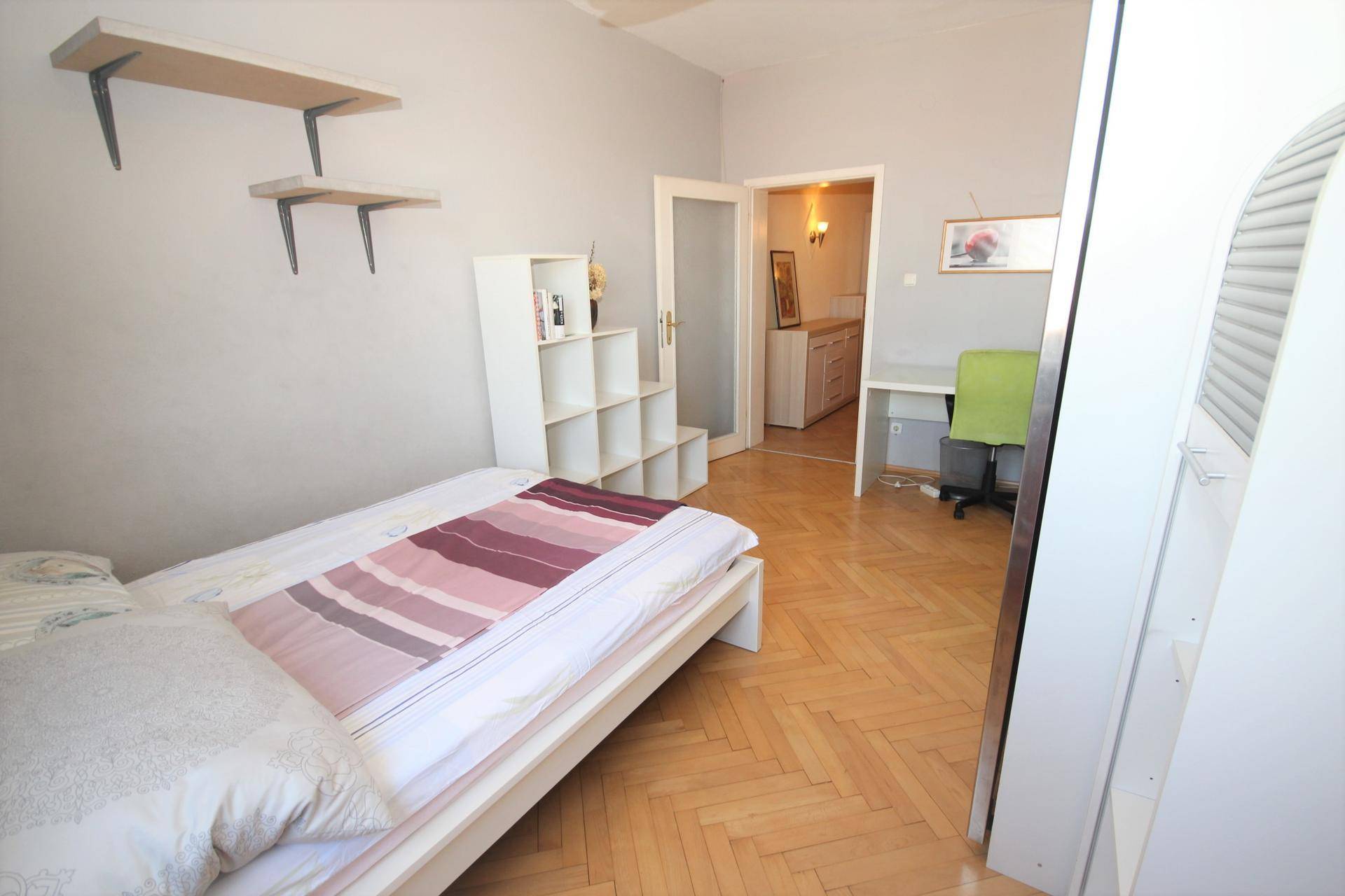 Schlafzimmer mit Einzelbett, Regalen und Blick in den Flur.