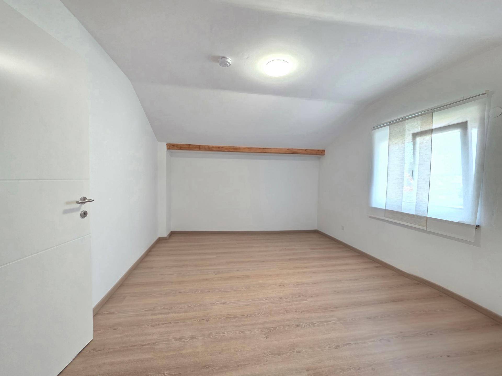 Leeres Gästezimmer im Dachgeschoss mit schrägen Wänden und Holzbalken.
