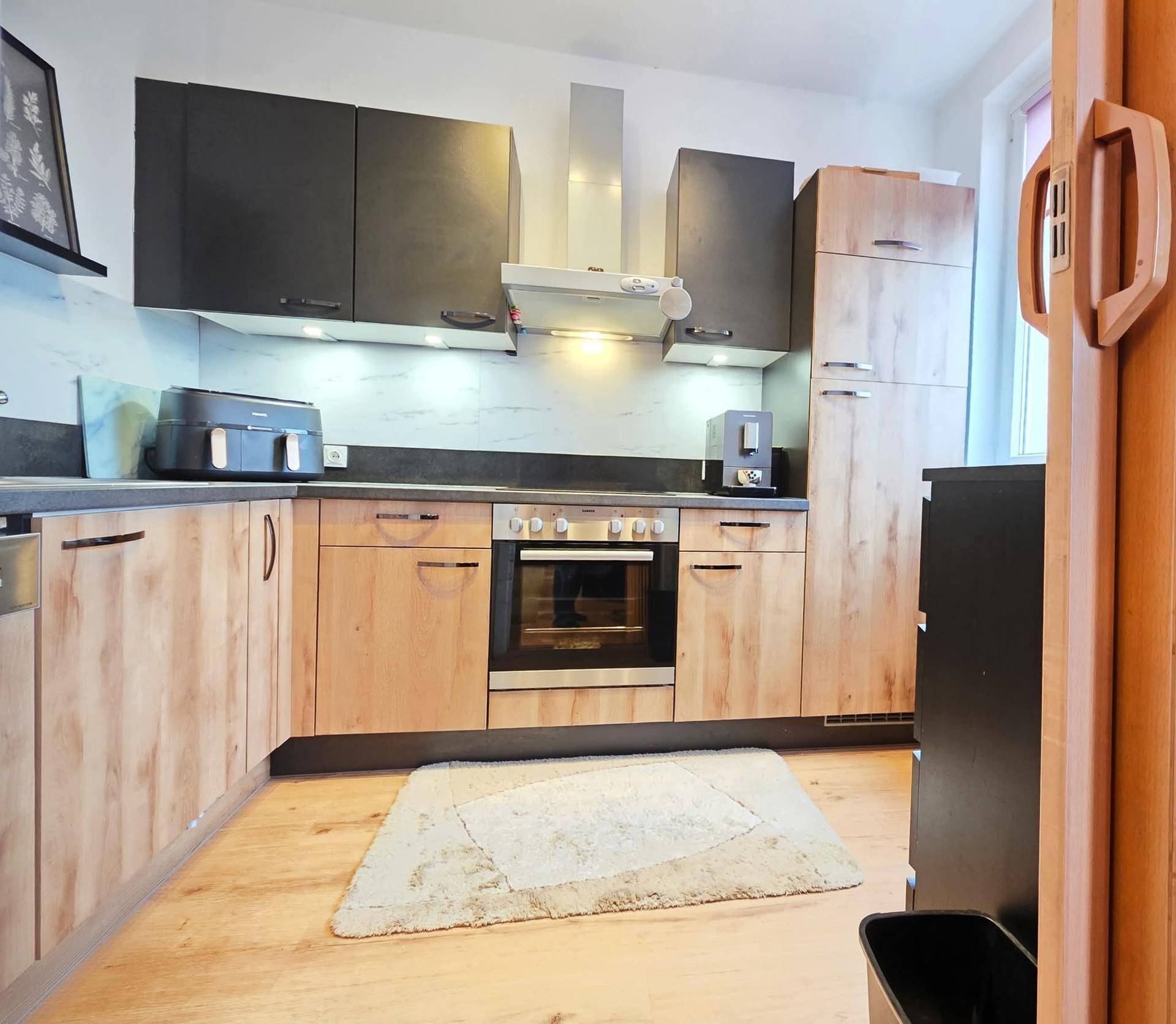 Moderne Küche mit Holz- und dunklen Schränken, integriertem Backofen und Dunstabzugshaube.