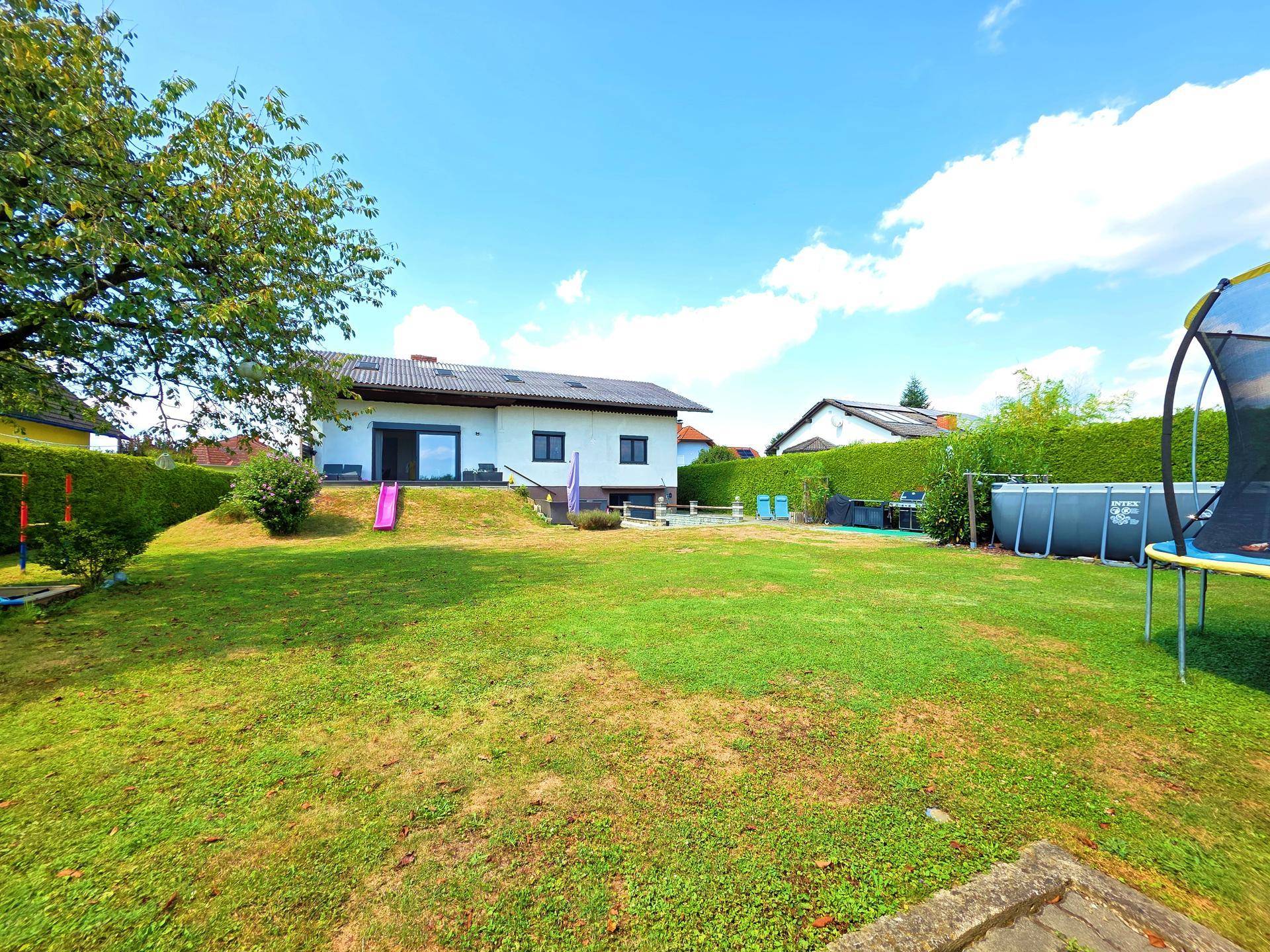 Großer Garten mit Rasenfläche, Trampolin und Rutsche, ideal für Familienaktivitäten.
