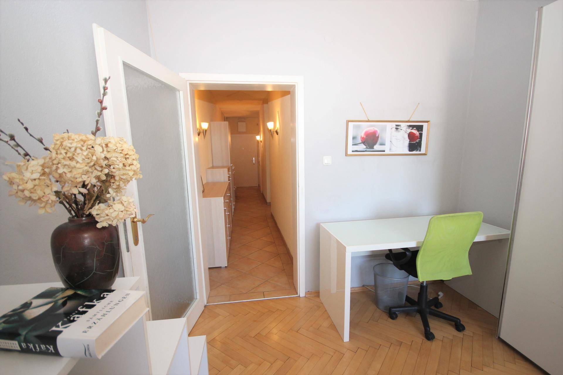 Eingangsbereich zu einem hellen Büro mit Schreibtisch und Parkettboden.