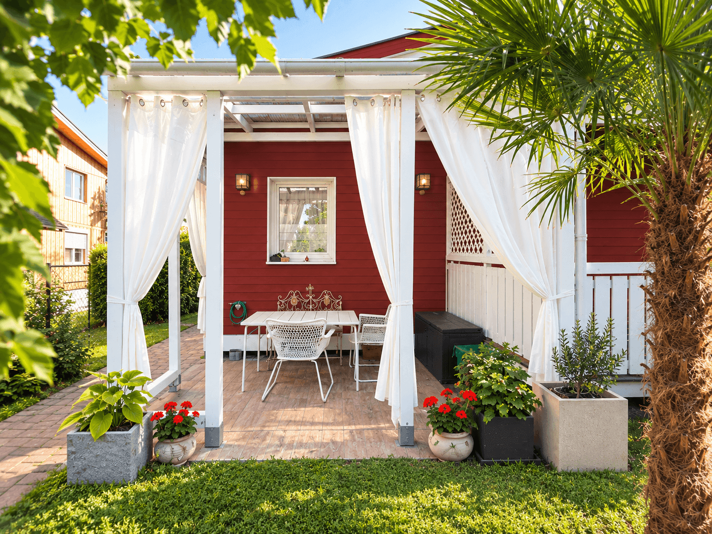 Überdachte Terrasse mit weißen Vorhängen, Esstisch und Blick in den grünen Garten.