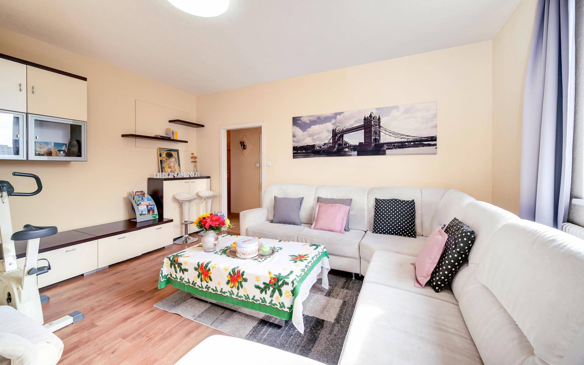 Gemütliches Wohnzimmer mit weißem Ecksofa, Holzboden und Heimtrainer.