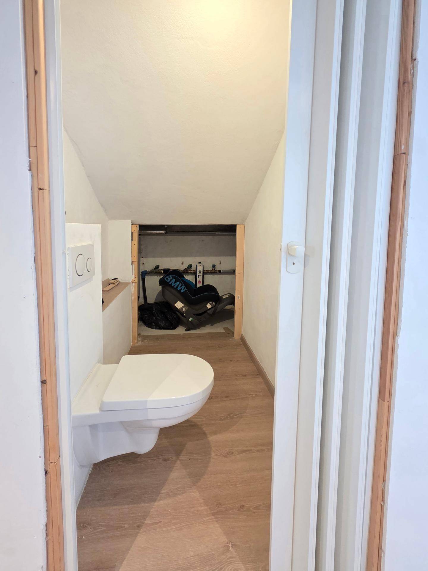 Kleines Gäste-WC mit wandhängender Toilette und Stauraum im Hintergrund.