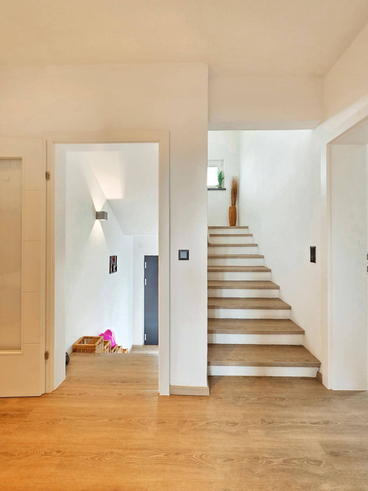 Heller Flur mit Holztreppe und modernem Laminatboden, der zu den oberen Etagen führt.