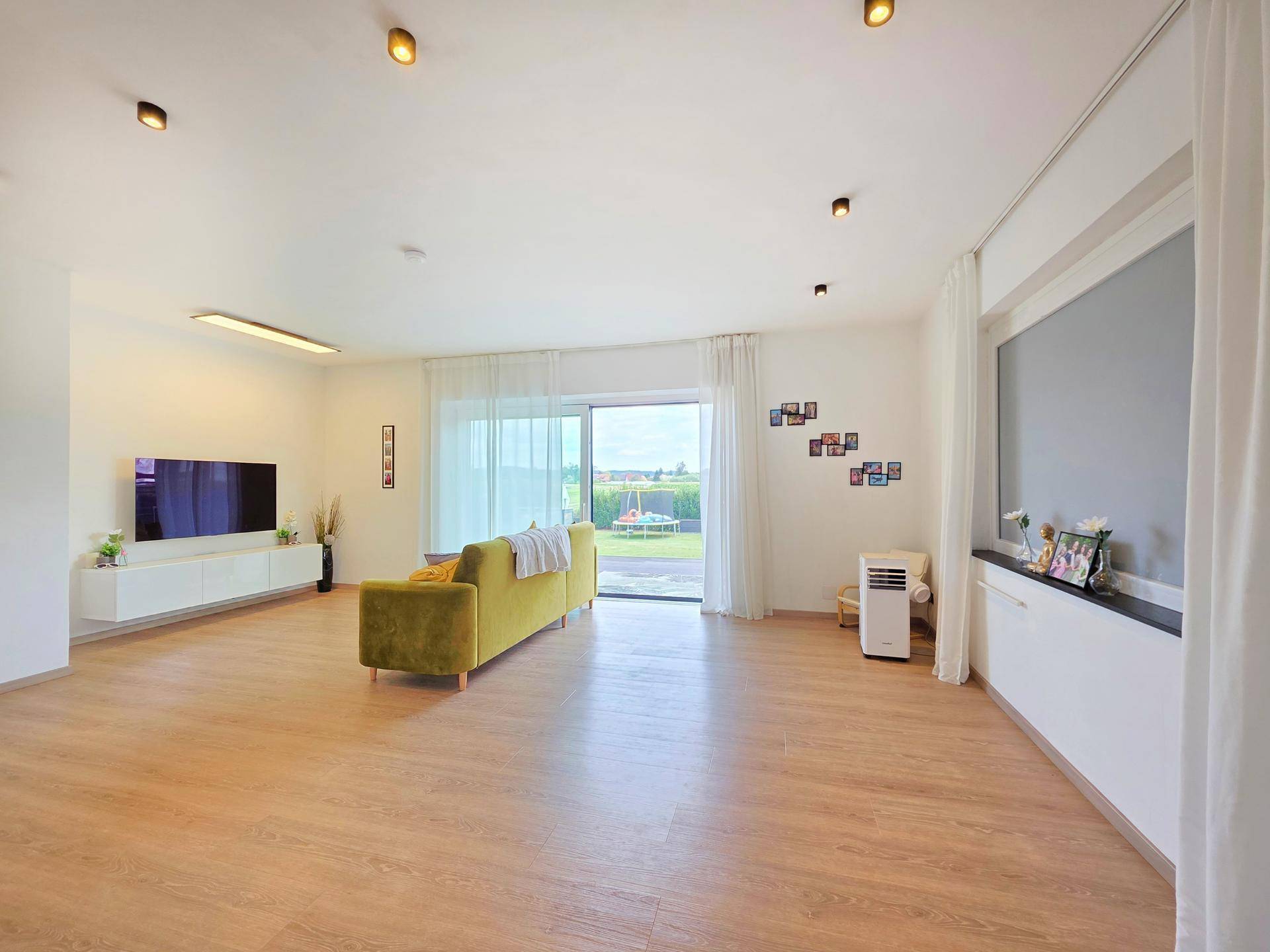 Weitläufiges Wohnzimmer mit viel Tageslicht, Laminatboden und Blick in den grünen Garten.