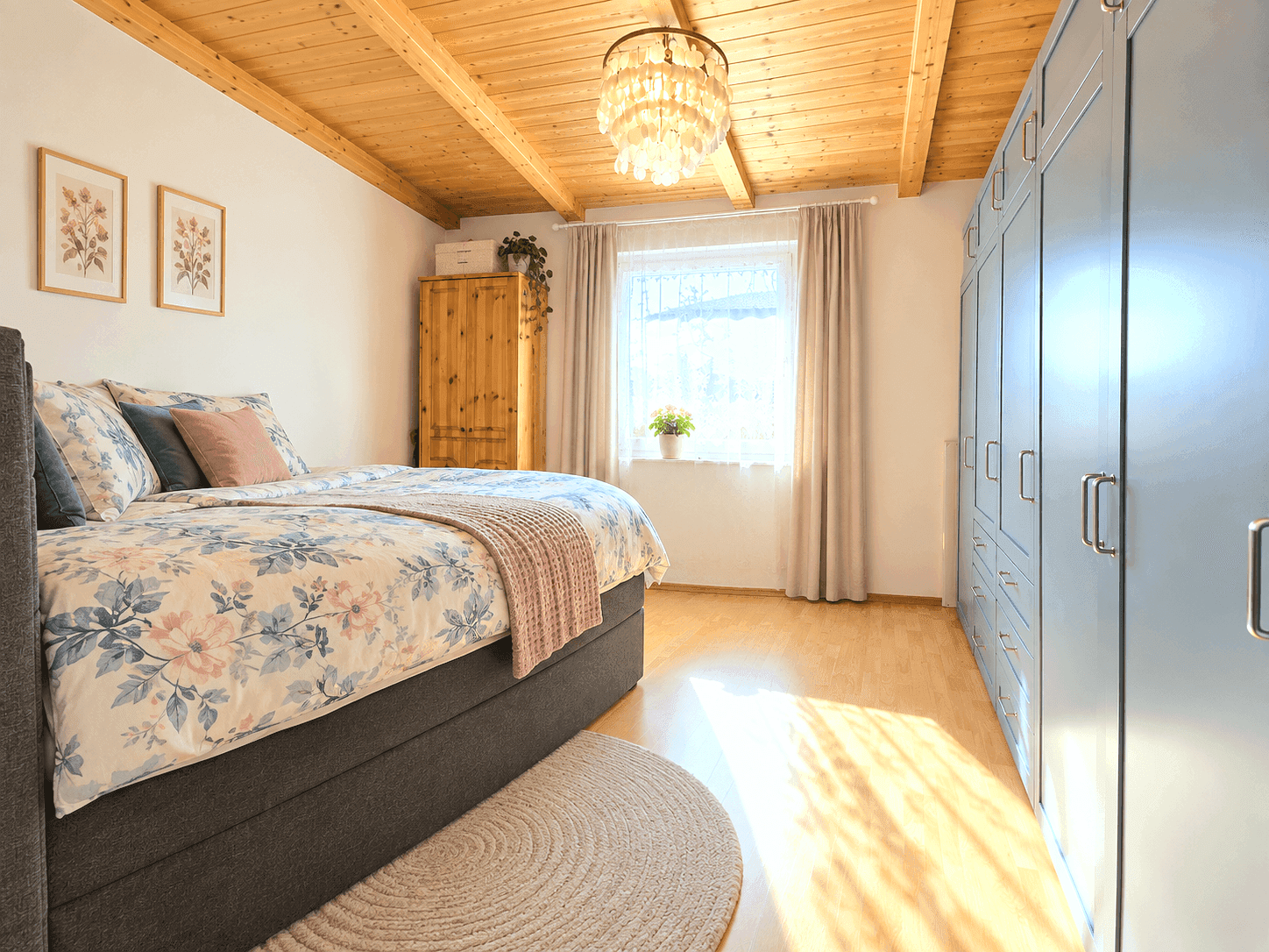 Schlafzimmer mit Holzbalkendecke, großem Fenster und blauen Einbauschränken.