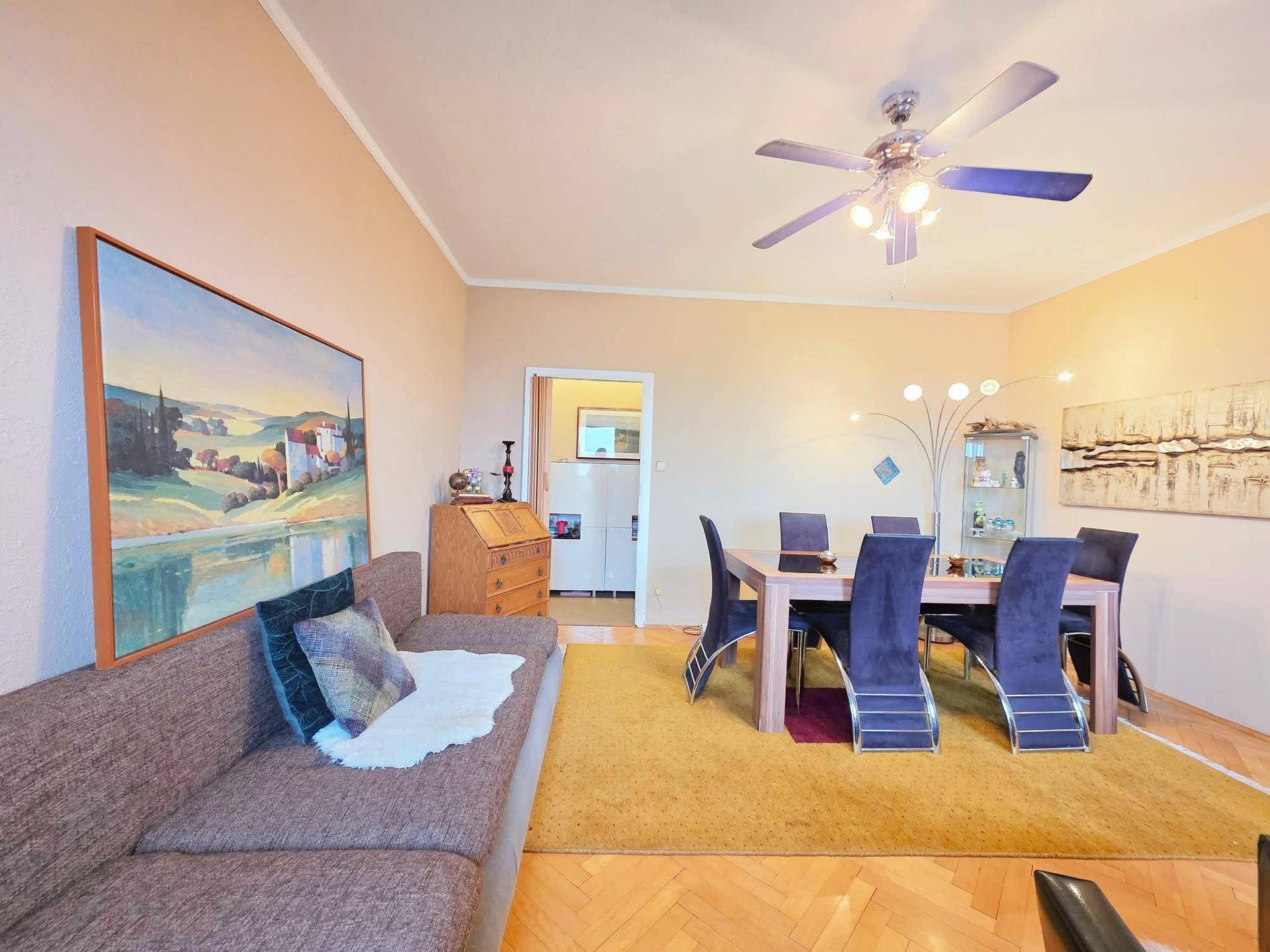 Wohn-Essbereich mit beigem Sofa, Holztisch und einem Deckenventilator, der für angenehme Luft sorgt.