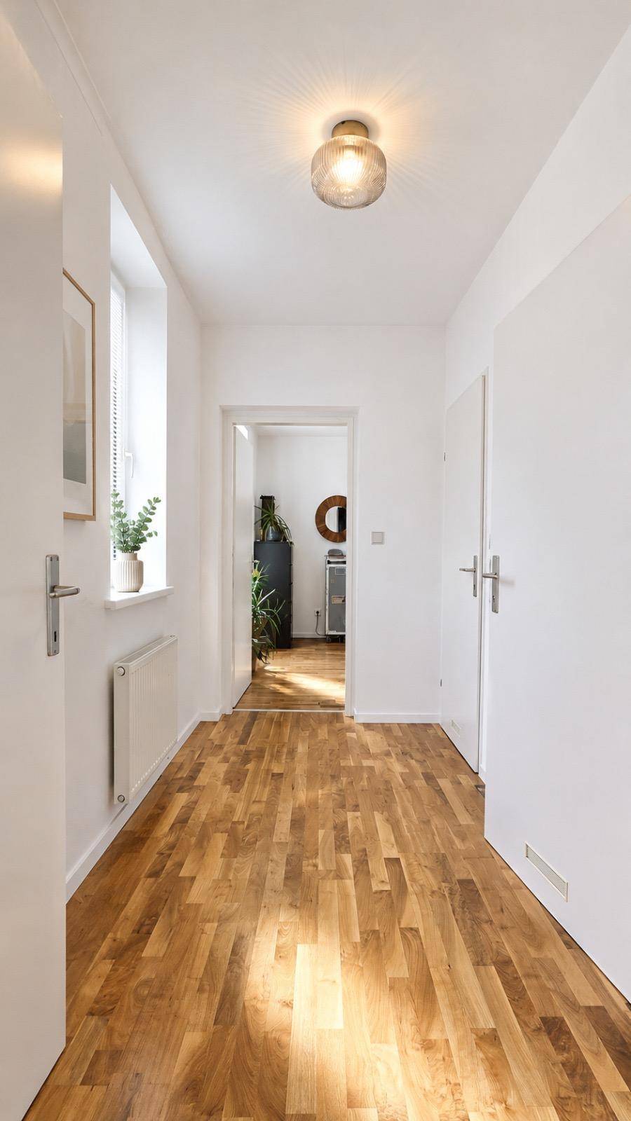 Heller Flur mit Holzboden, Fenster und Zugang zu verschiedenen Zimmern.