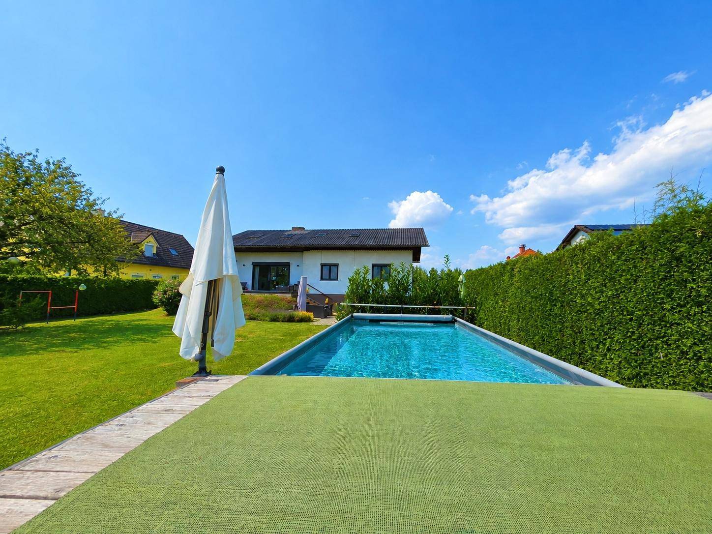 Weitläufiger Garten mit privatem Pool und Liegewiese, umgeben von einer grünen Hecke.