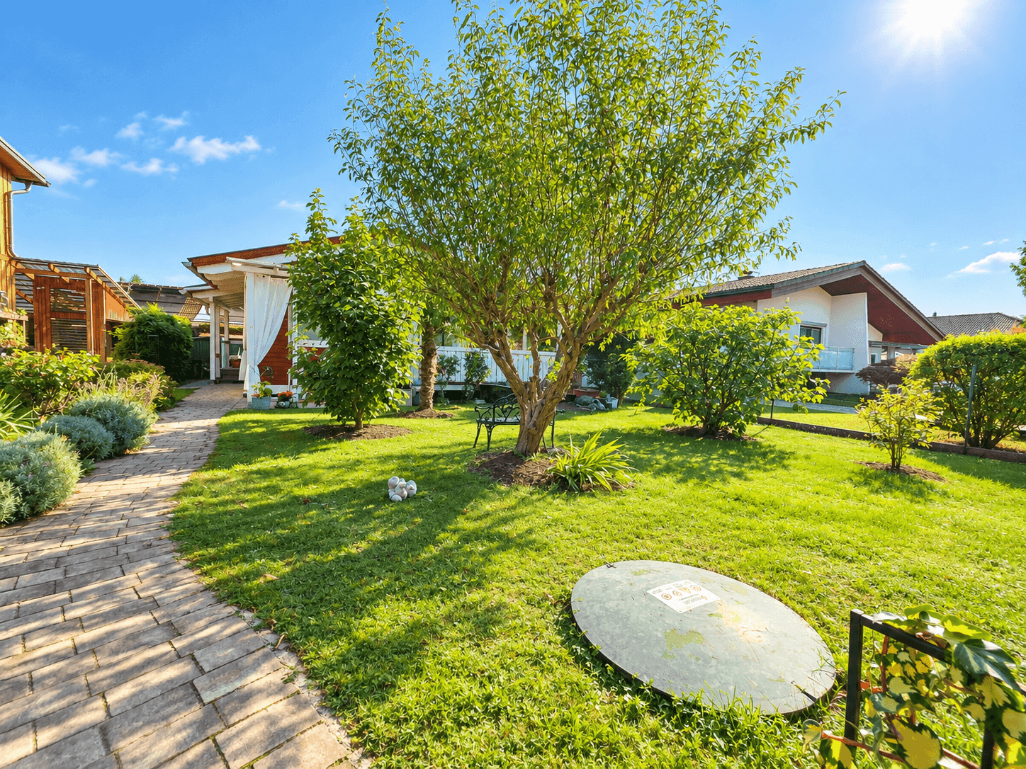 Weitläufiger Garten mit Rasen, Bäumen und einem gepflasterten Weg zum Haus.