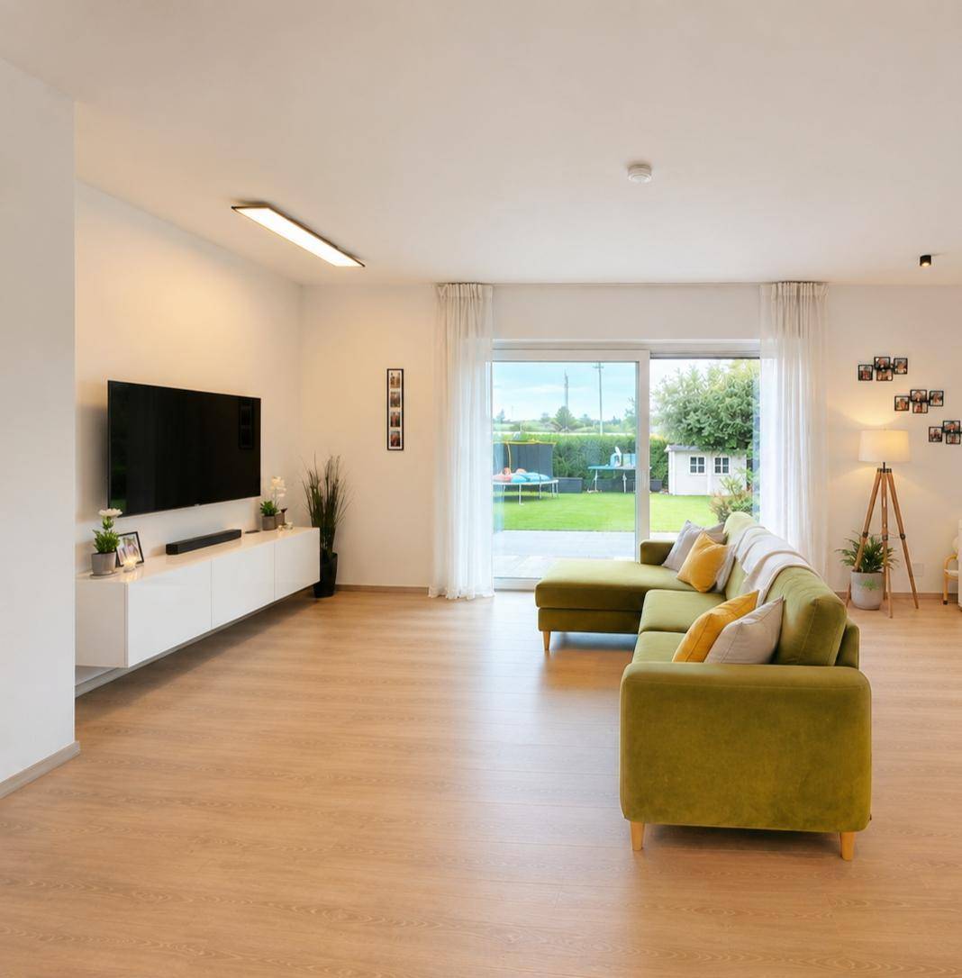 Helles Wohnzimmer mit Laminatboden, großem Sofa und Zugang zur Terrasse mit Gartenblick.