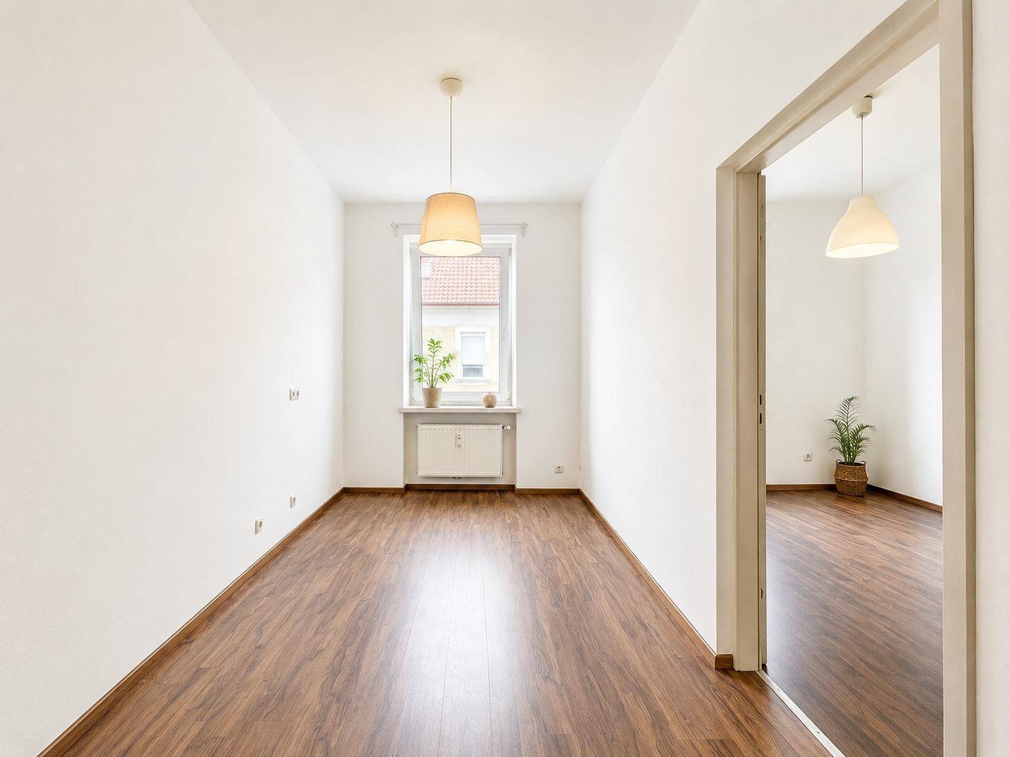 Langer, heller Raum mit einem Fenster, Holzboden und weiß gestrichenen Wänden.
